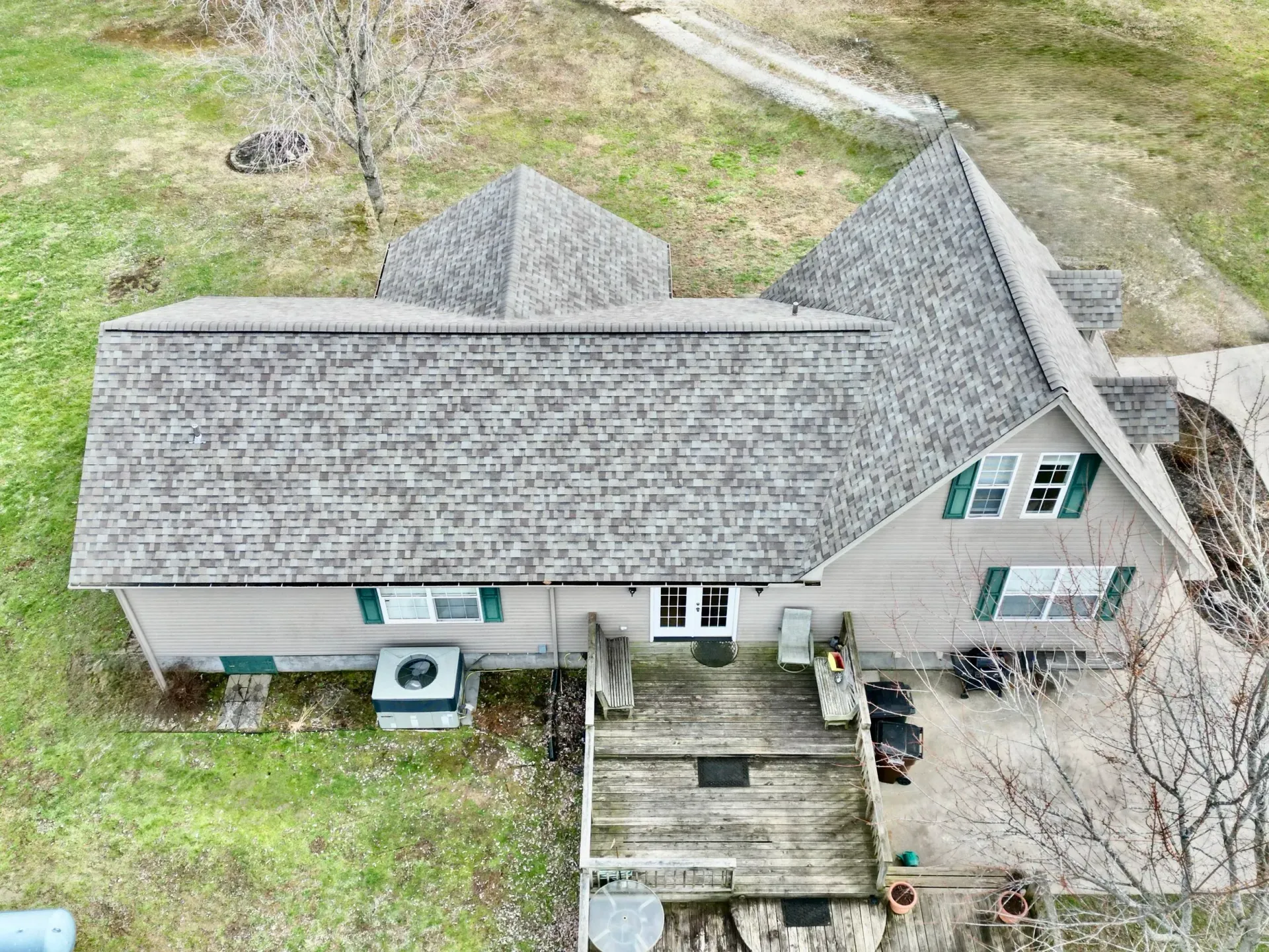 Aerial view of a gray-roofed house with a wooden deck and small yard.