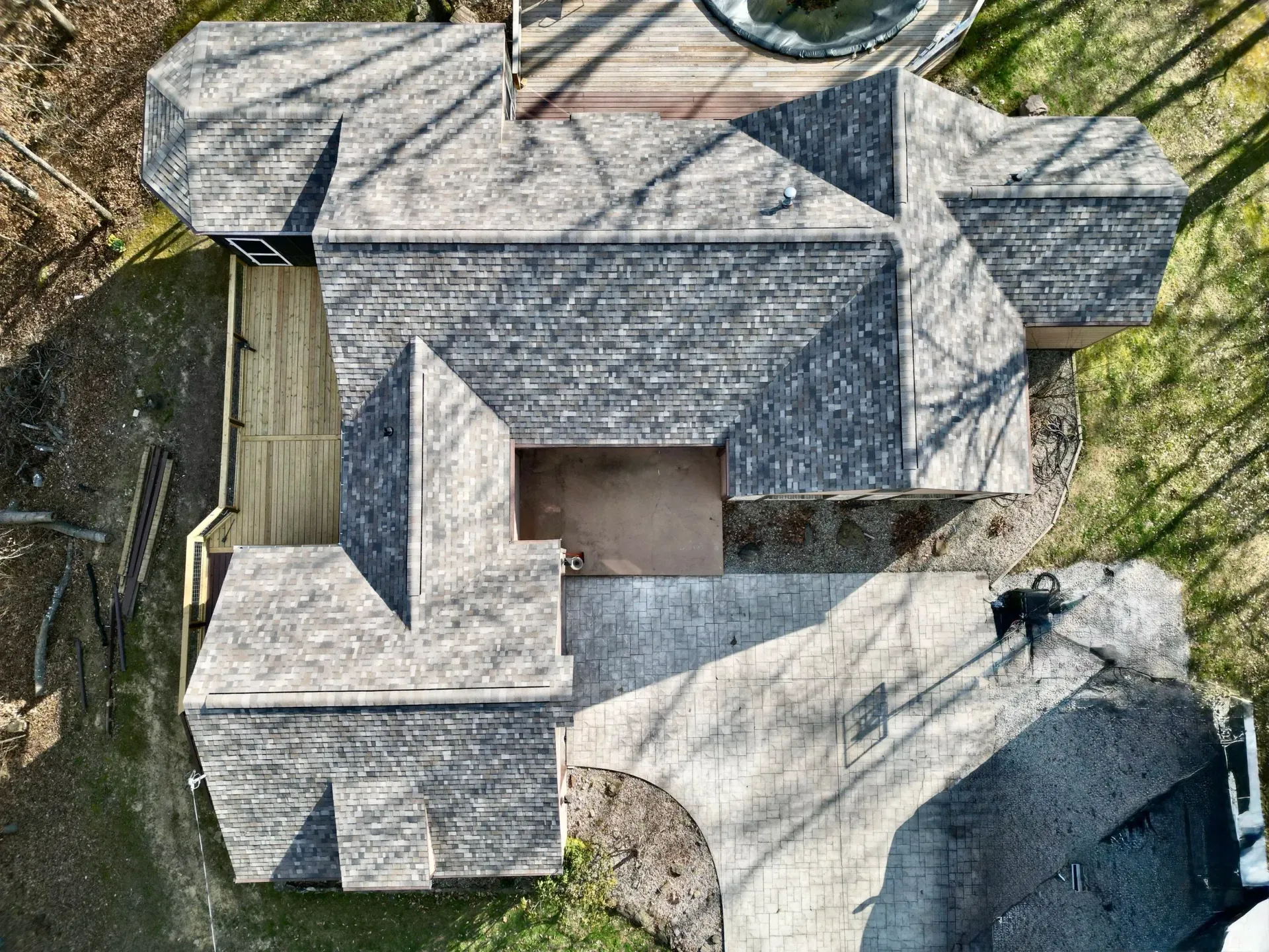 Aerial view of a house with gray shingle roofs, a central courtyard, and a curved driveway bordered by trees.