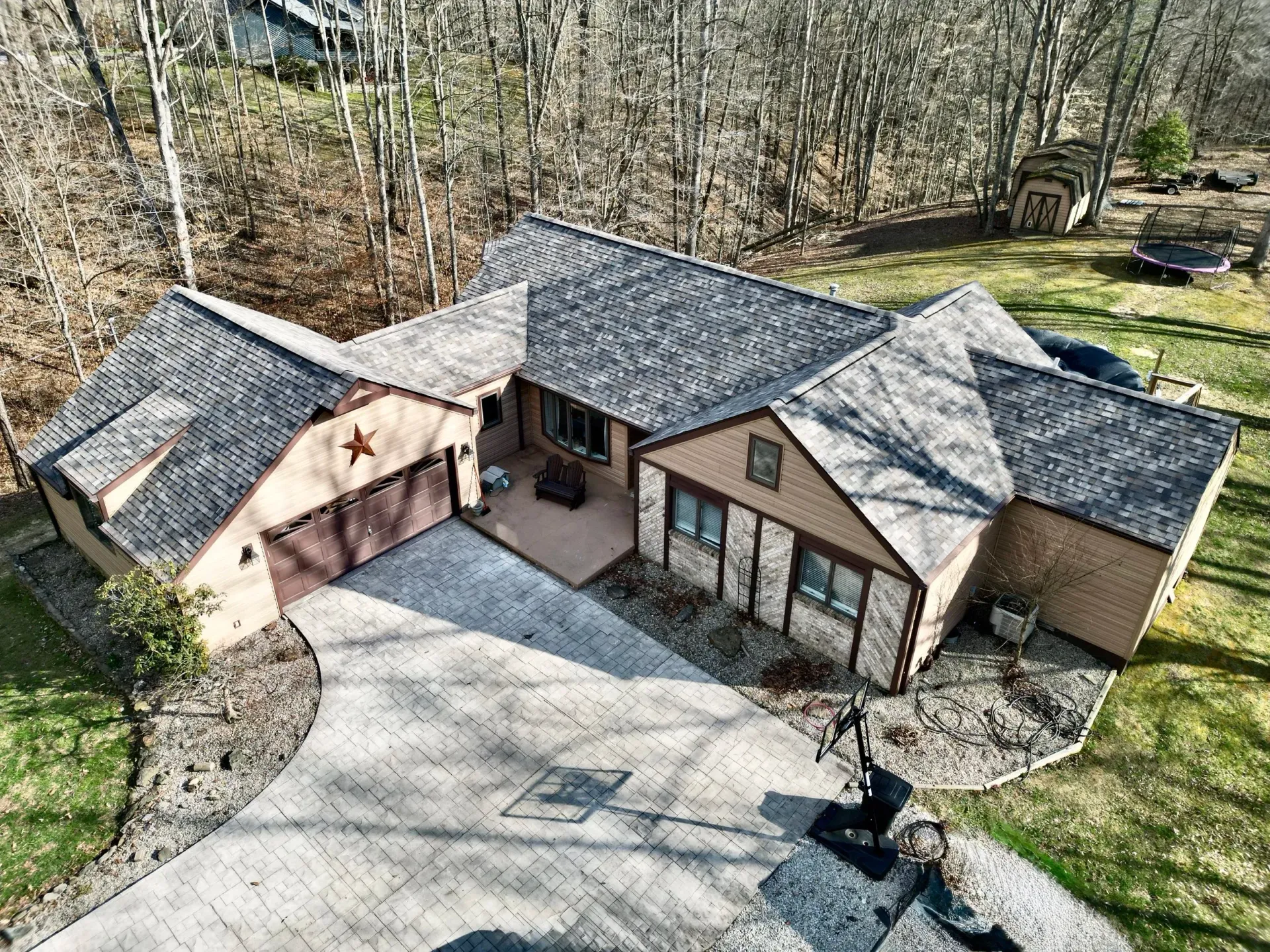 Aerial view of a suburban house with a large driveway, gray roof, and surrounding trees.