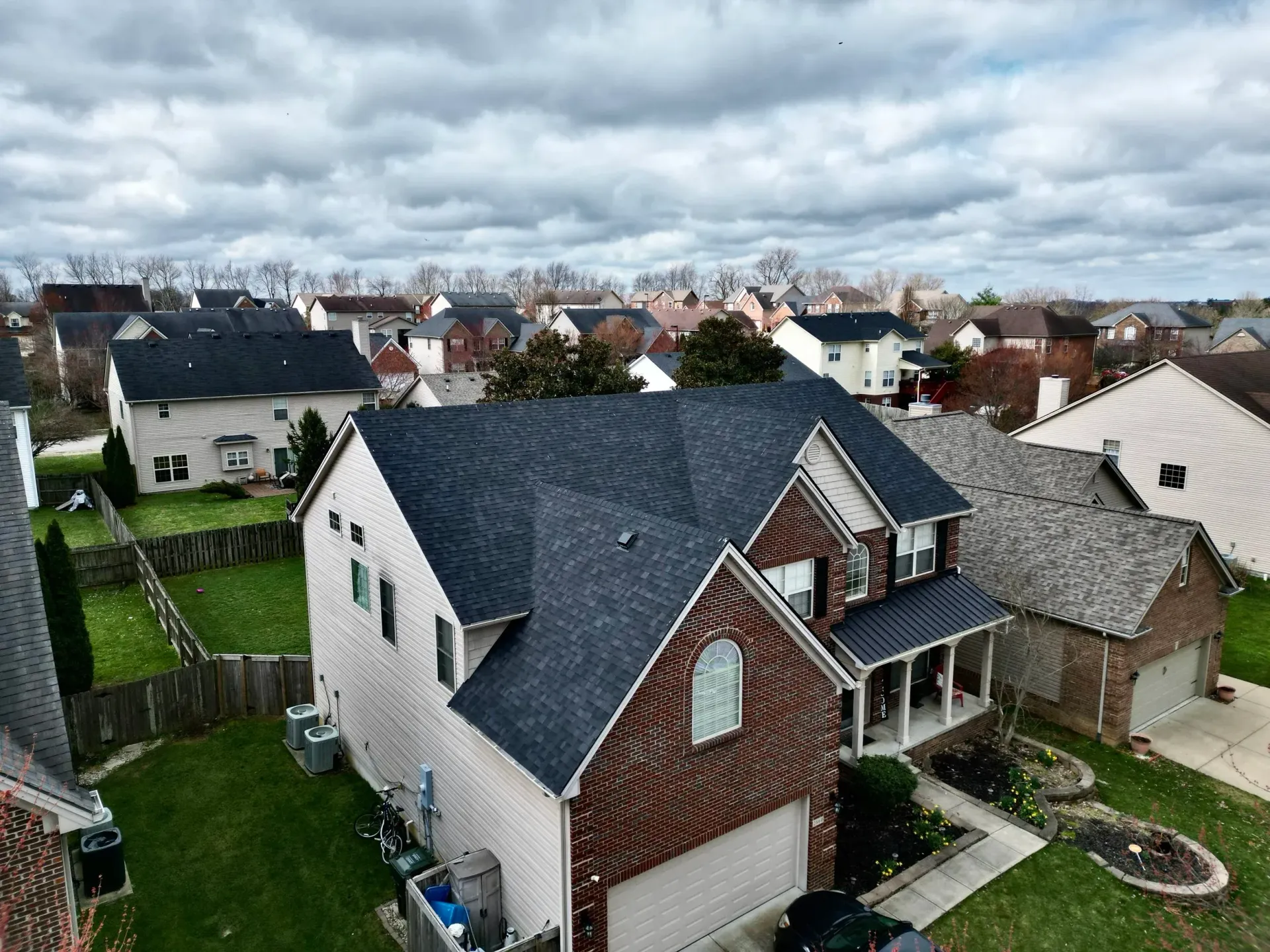 Suburban houses with dark roofs under a cloudy sky, viewed from above