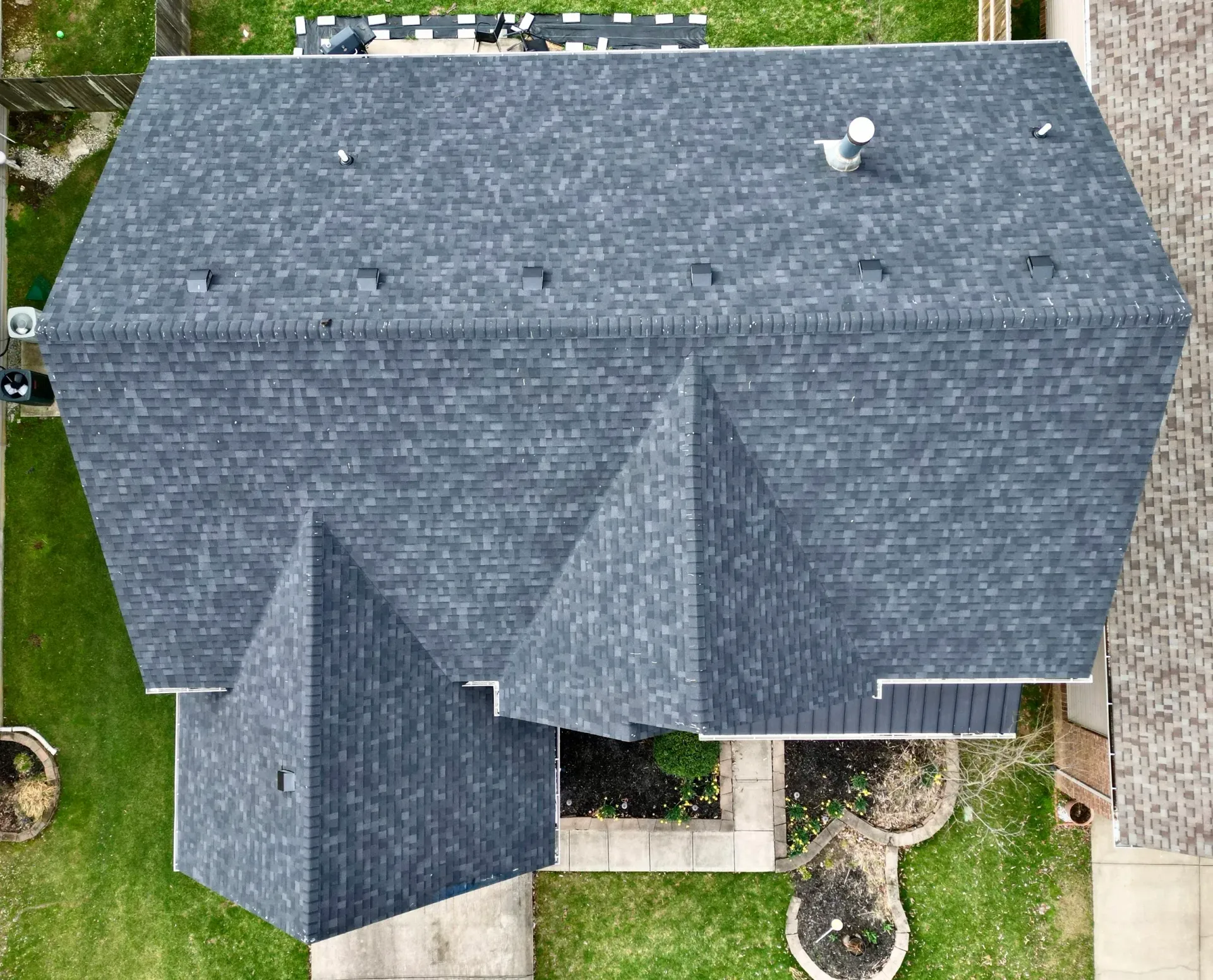Aerial view of a gray-shingled house roof with dormers and a small backyard