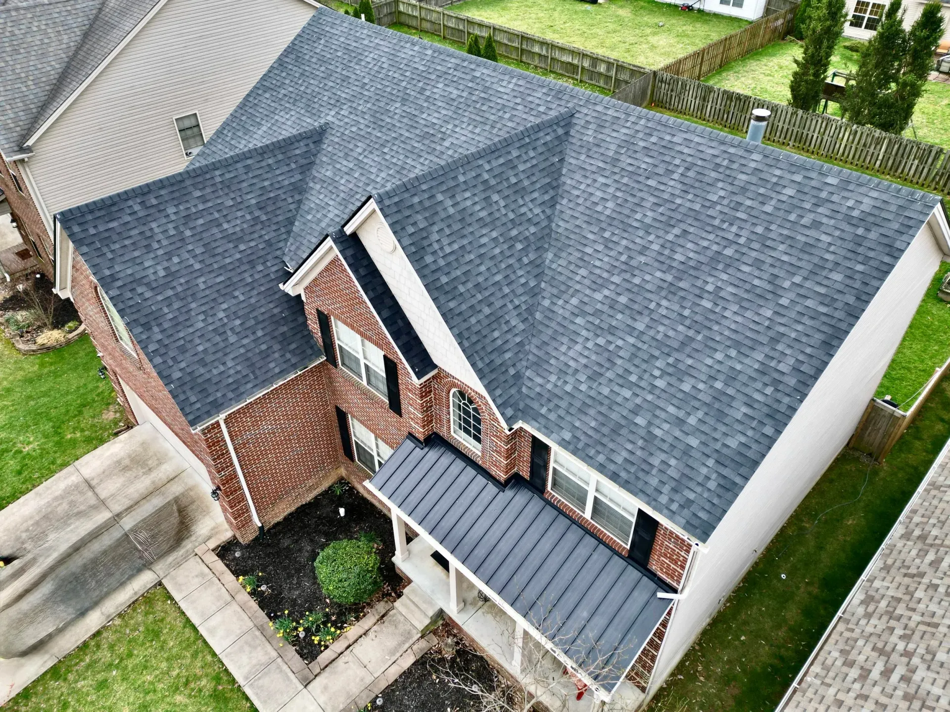 Aerial view of a two-story brick house with a gray shingled roof and small front porch.