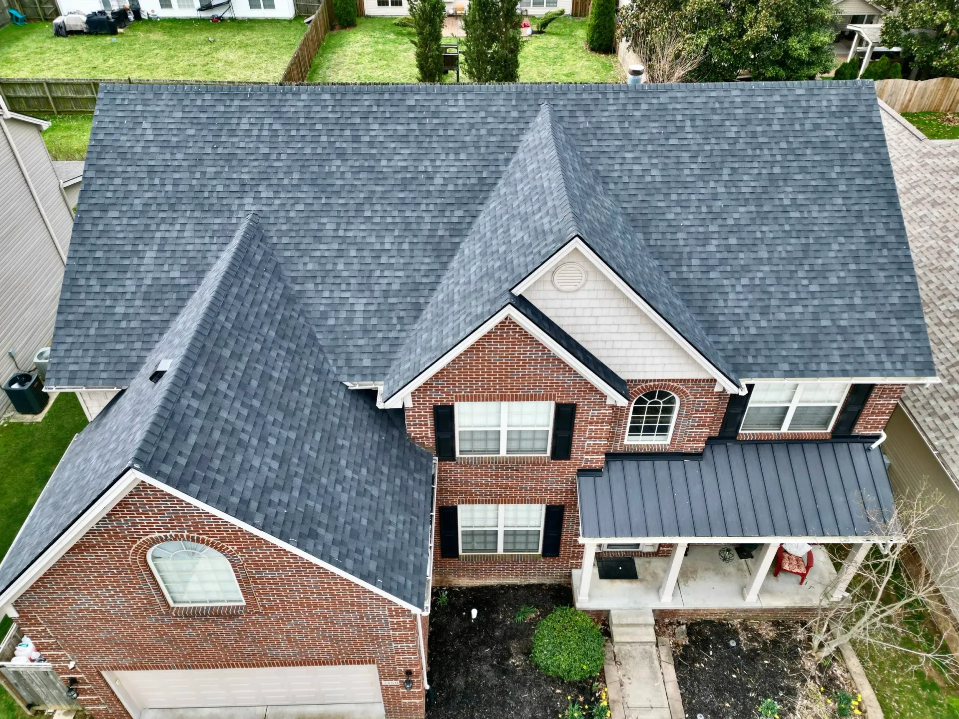 Aerial view of a two-story brick house with a dark gray roof and front porch in a suburban neighborhood