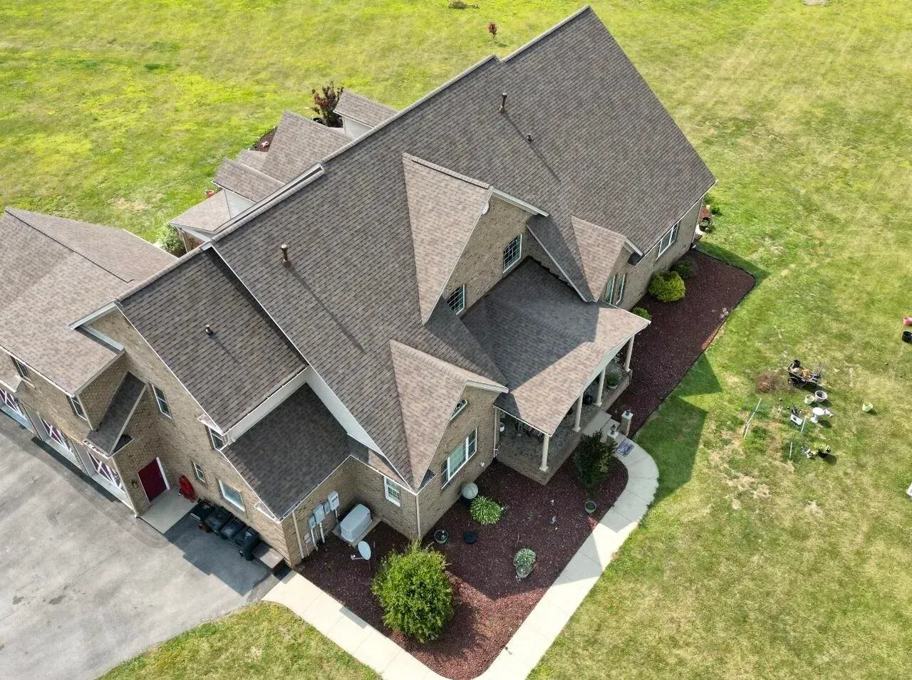 Aerial view of a large gray-roofed suburban house with a lawn and landscaped front yard.
