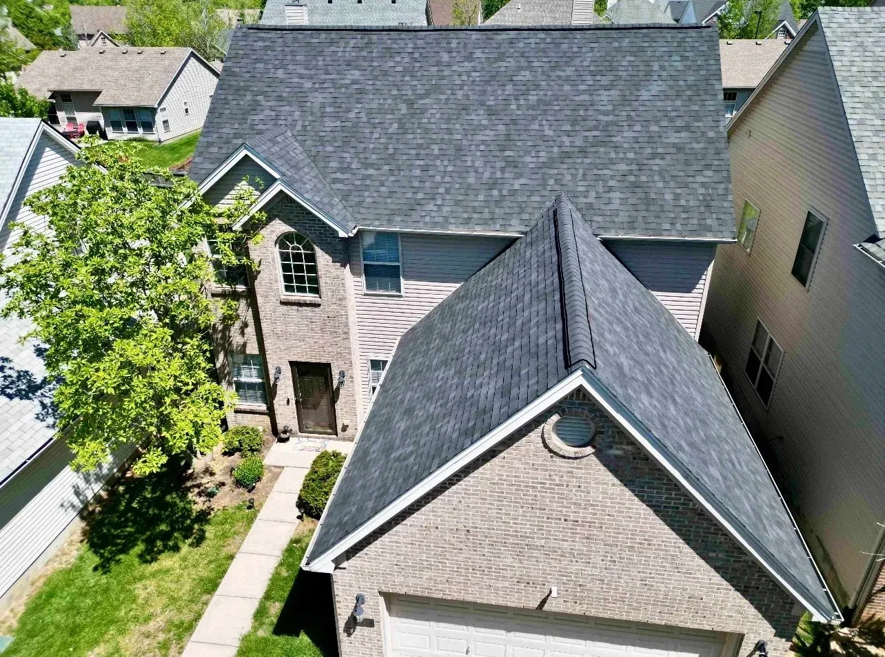 Aerial view of a gray-roofed house with a brick exterior and a leafy tree in the front yard