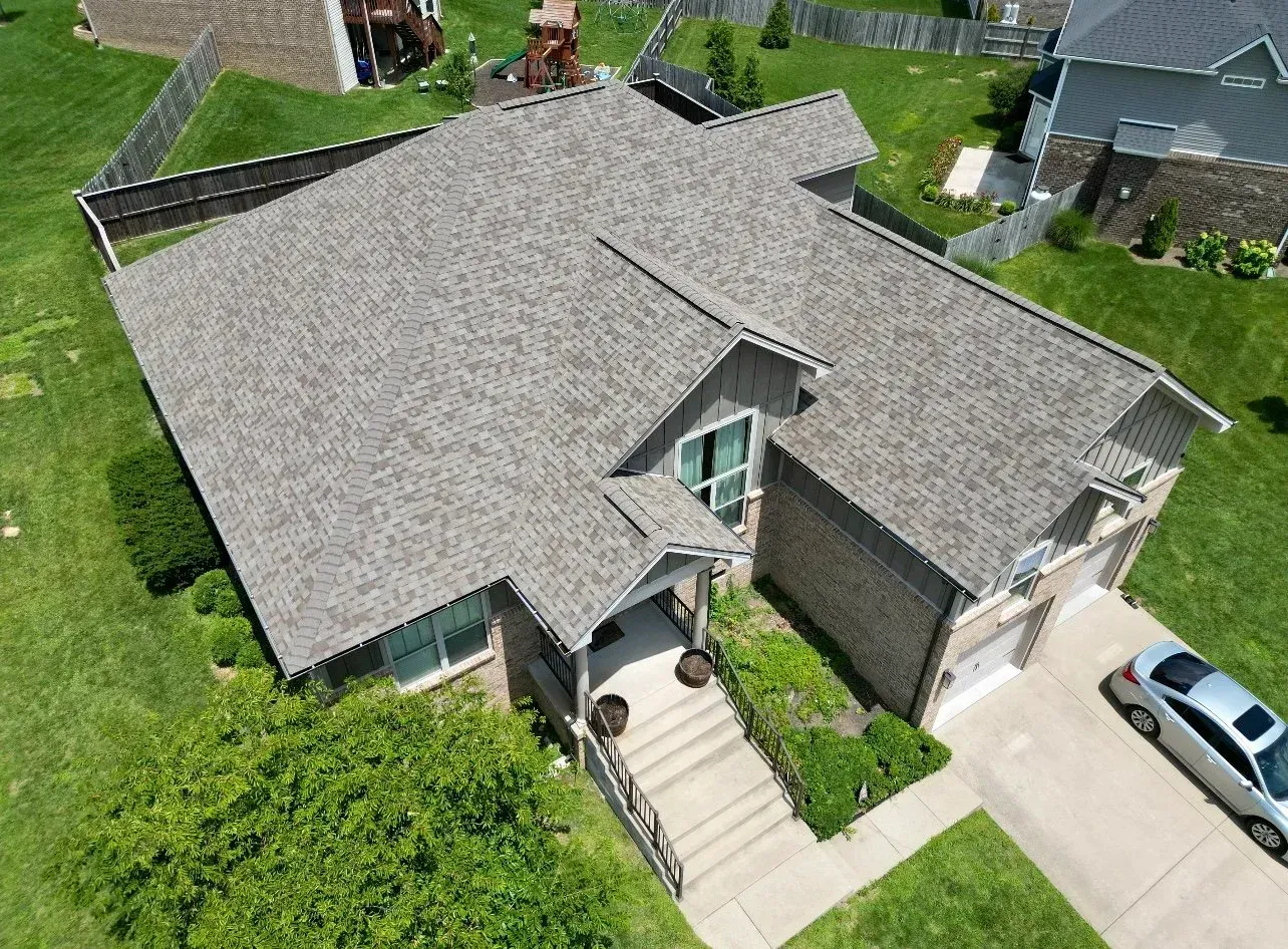 Aerial view of a gray-roofed suburban house with a front walkway, lawn, and driveway.