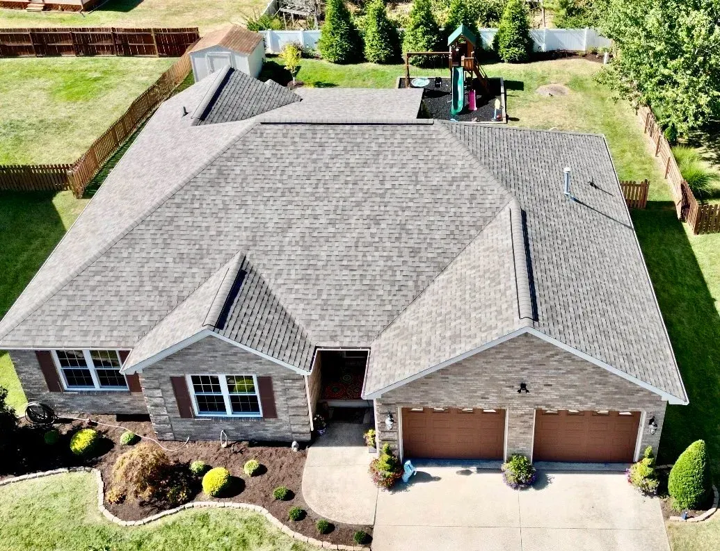 Aerial view of a brick suburban house with a gray roof, two-car garage, and landscaped front yard