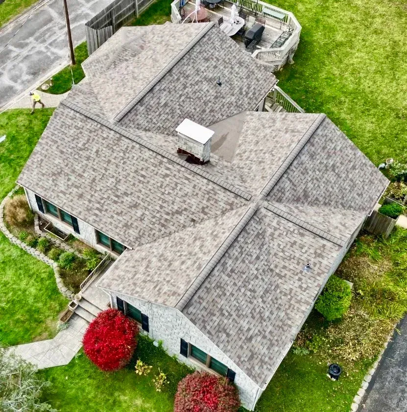 Aerial view of a gray shingled house with a green lawn and a red bush near the front steps.