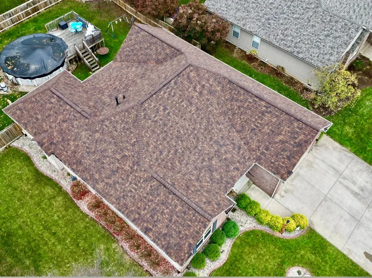 Aerial view of a brown-roofed house with a driveway, lawn, and backyard pool.