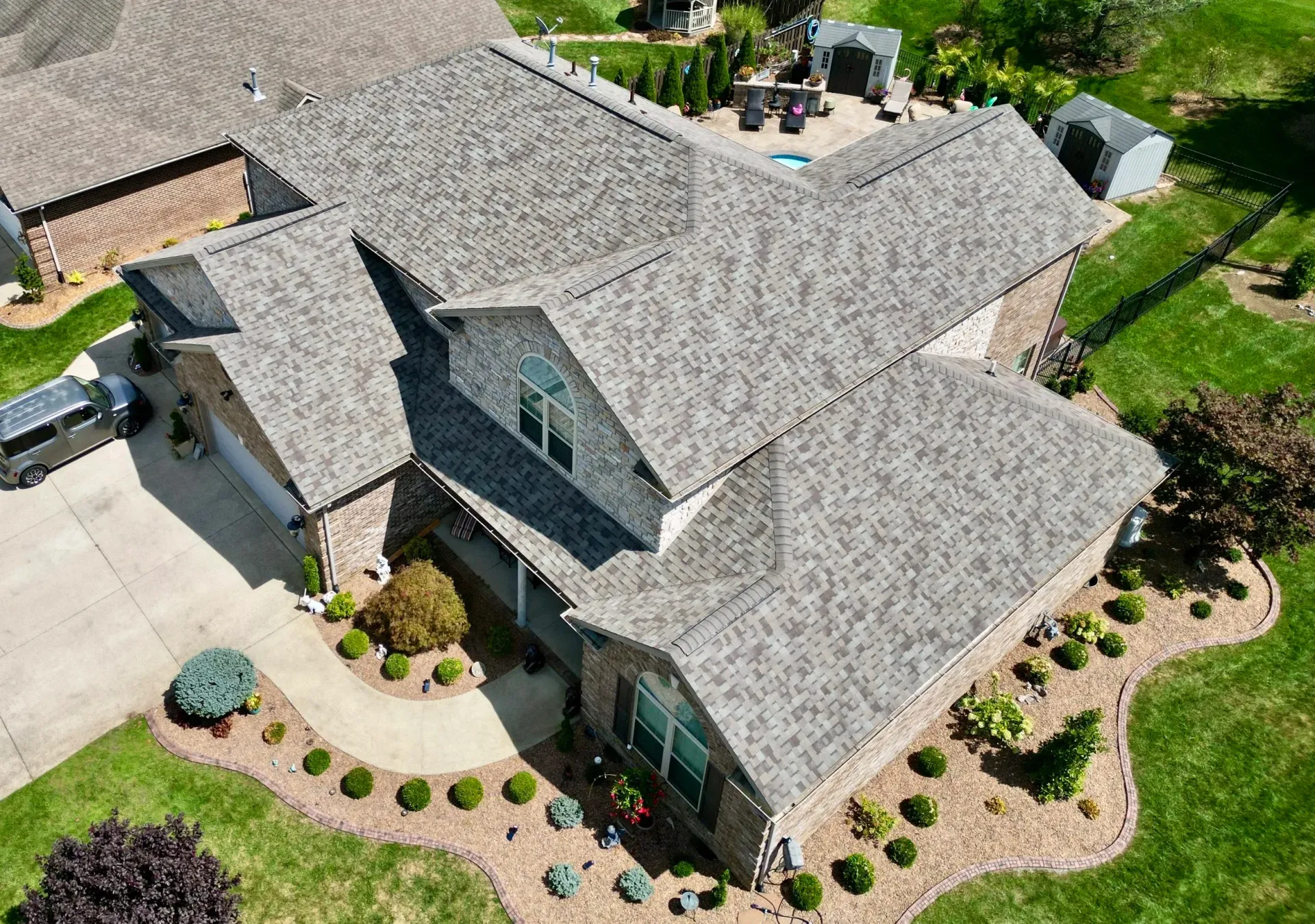 Aerial view of a gray-roofed suburban house with a landscaped front yard and driveway.