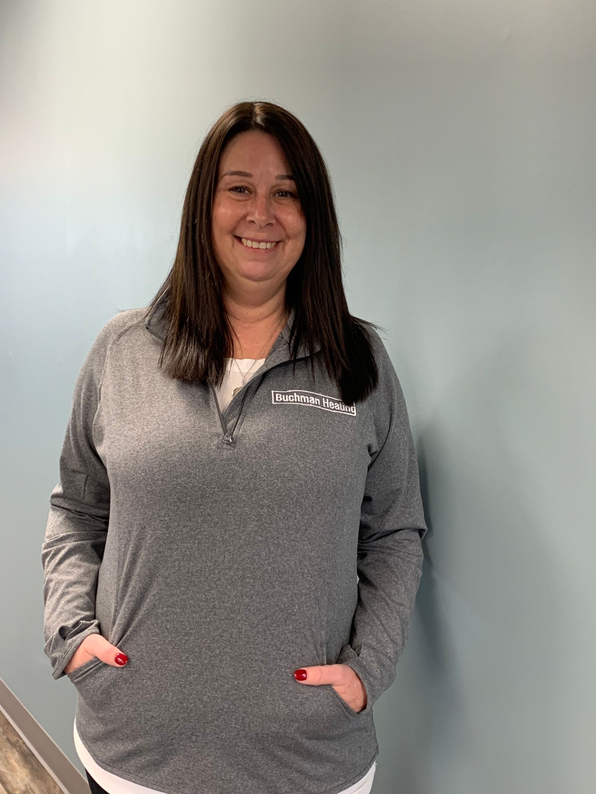 A woman is standing in front of a blue wall with her hands in her pockets.