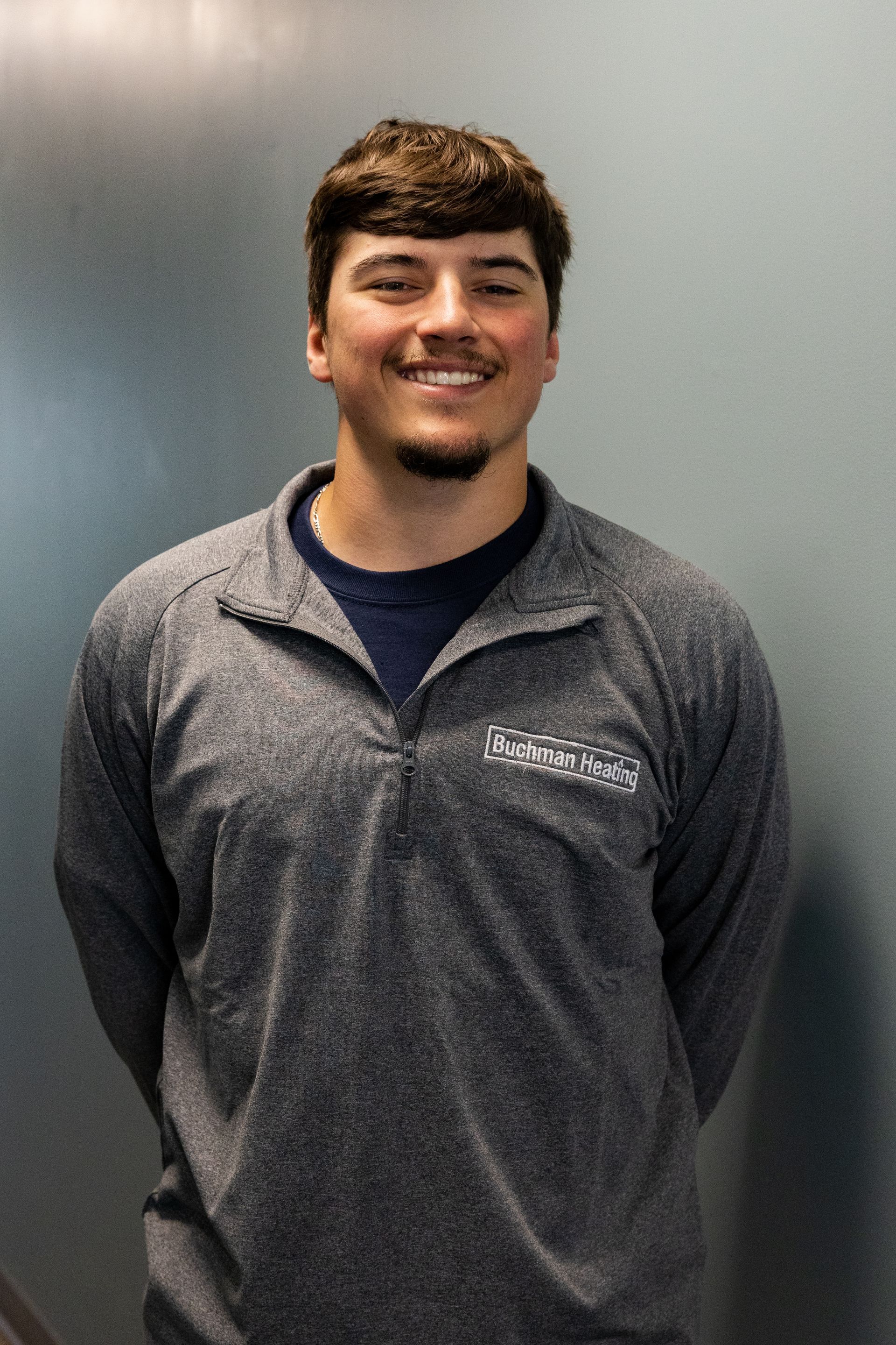 A young man wearing a gray shirt and a blue shirt is standing in front of a blue wall.