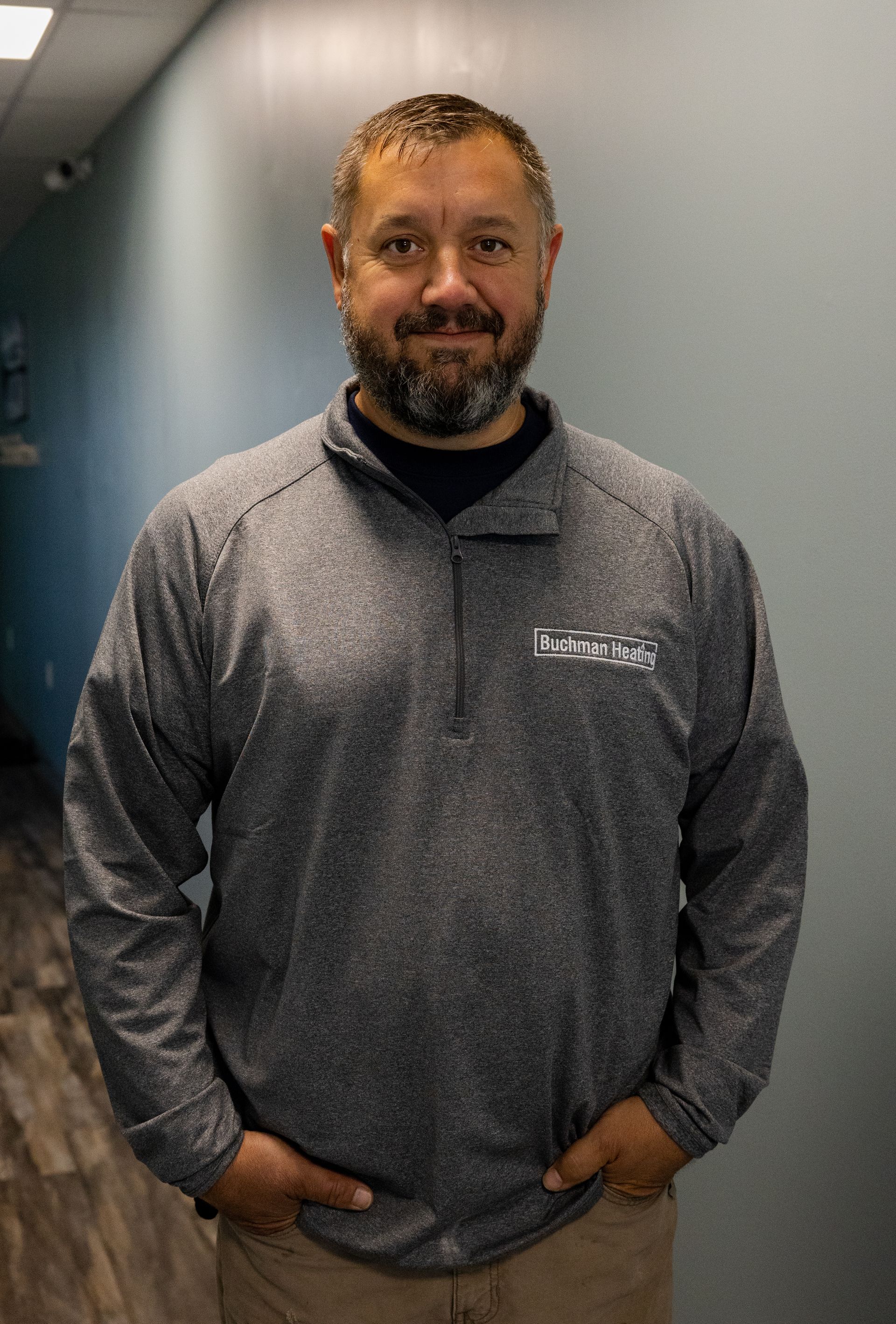 A man with a beard is standing in a hallway with his hands in his pockets.