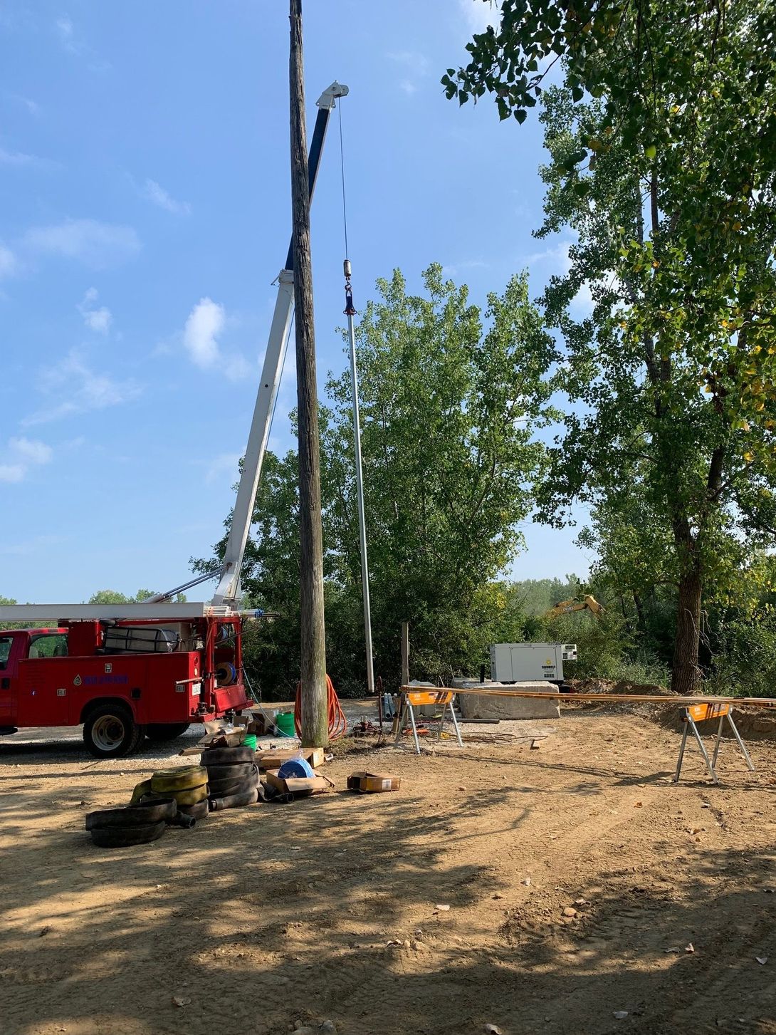 Red truck with a lift assisting with work on a utility pole under a blue sky.