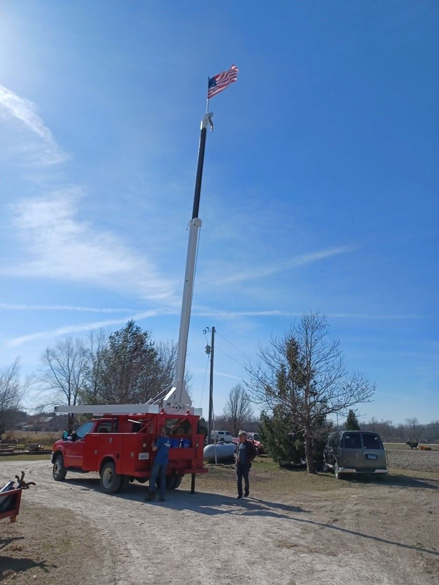 Red truck with a long arm holding an American flag high in the air; people standing nearby.