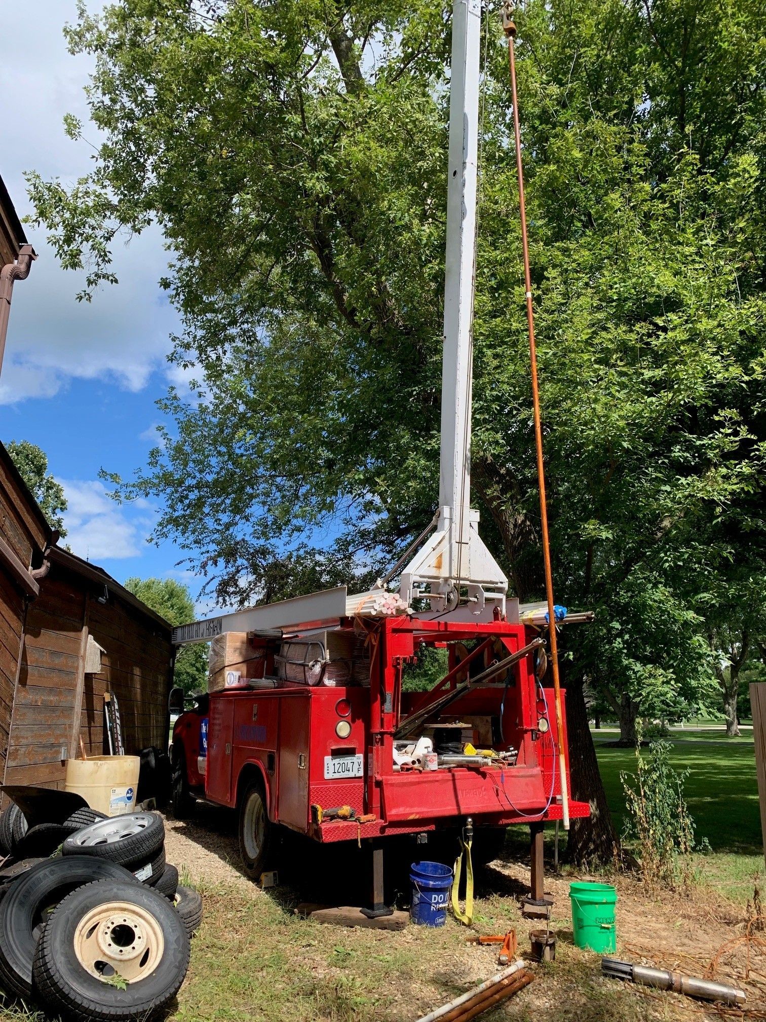 Red utility truck with an extended boom arm near a large tree in a yard.