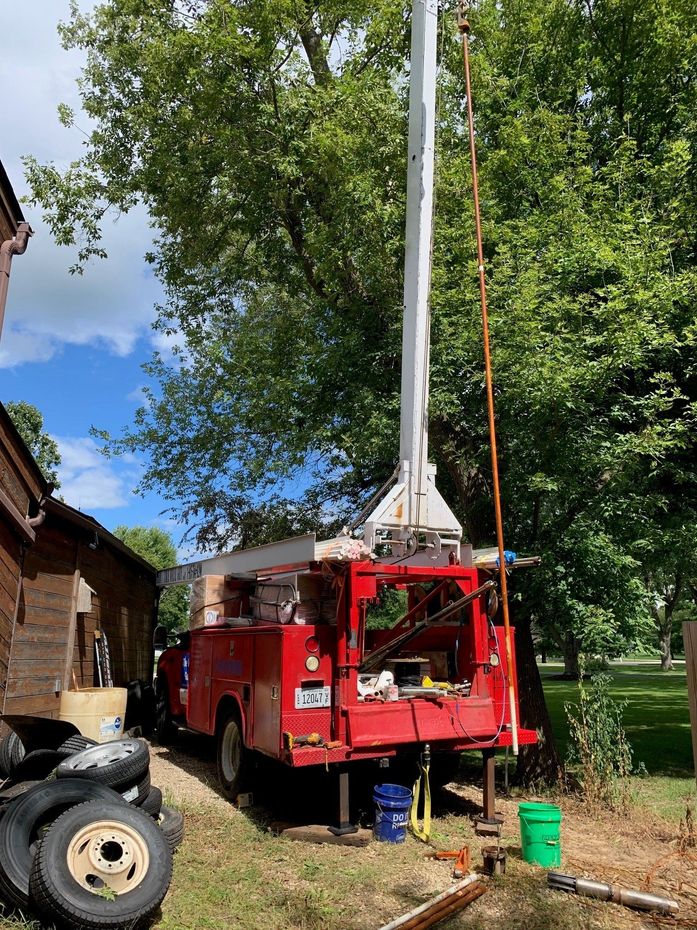 Red utility truck with an extended boom arm near a large tree in a yard.