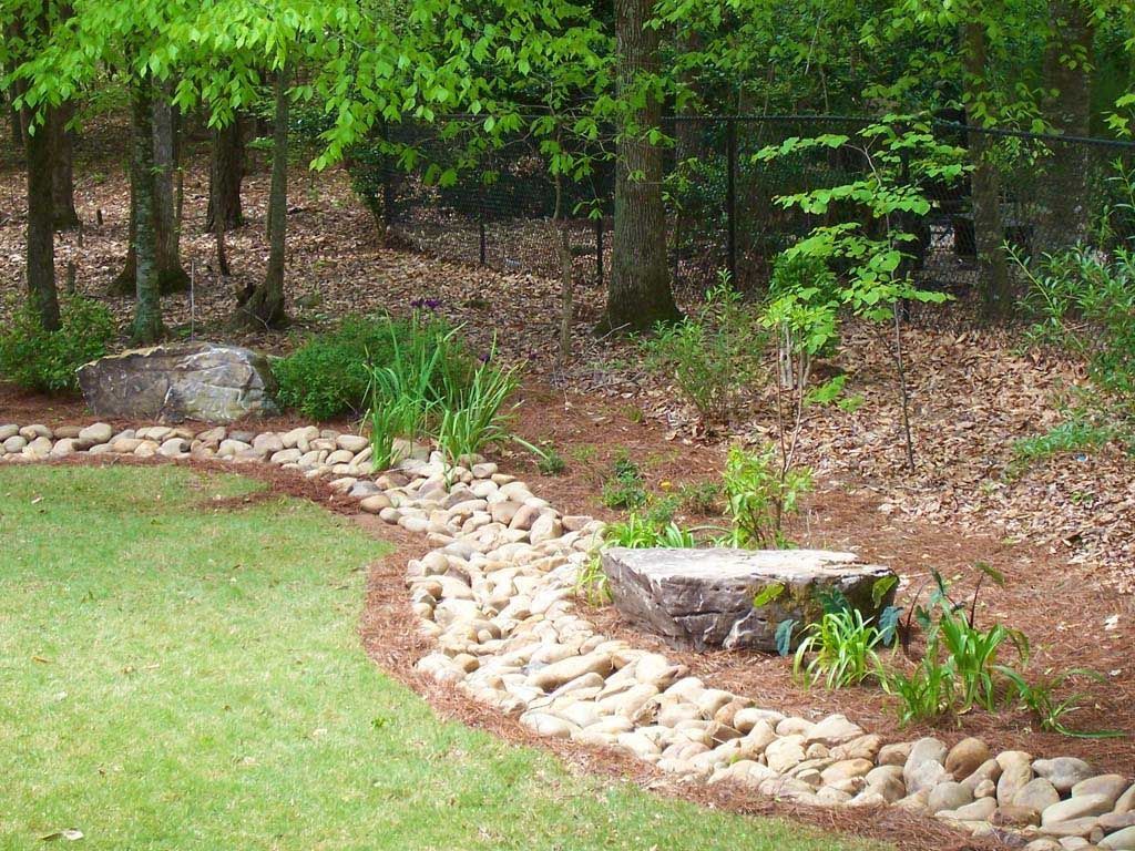 A landscaped garden with a rock-lined stream bed, trees, and lawn.