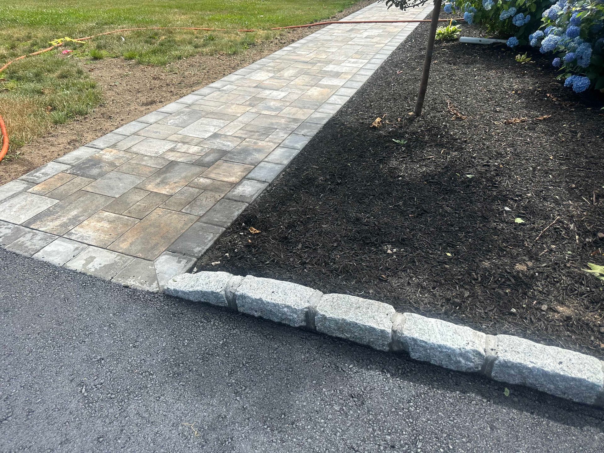 Brick walkway bordered by stone edging next to a mulched garden.
