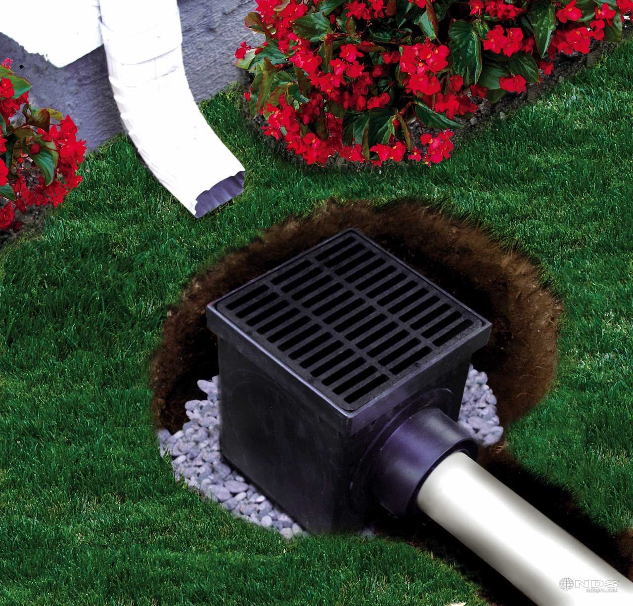 Drainage system with a black grate in a grassy yard, connected to a downspout and buried pipe.