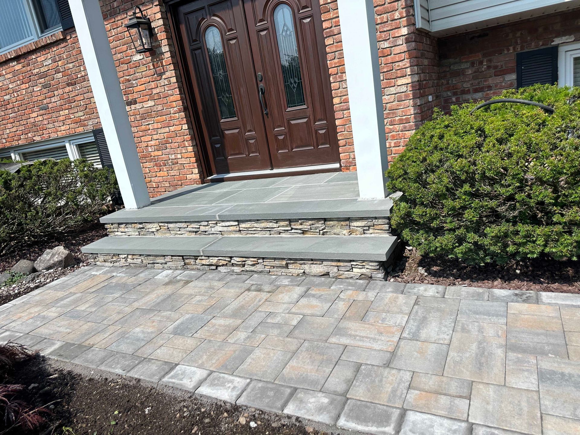 Brick facade with stone steps and walkway leading to a brown double door entrance.
