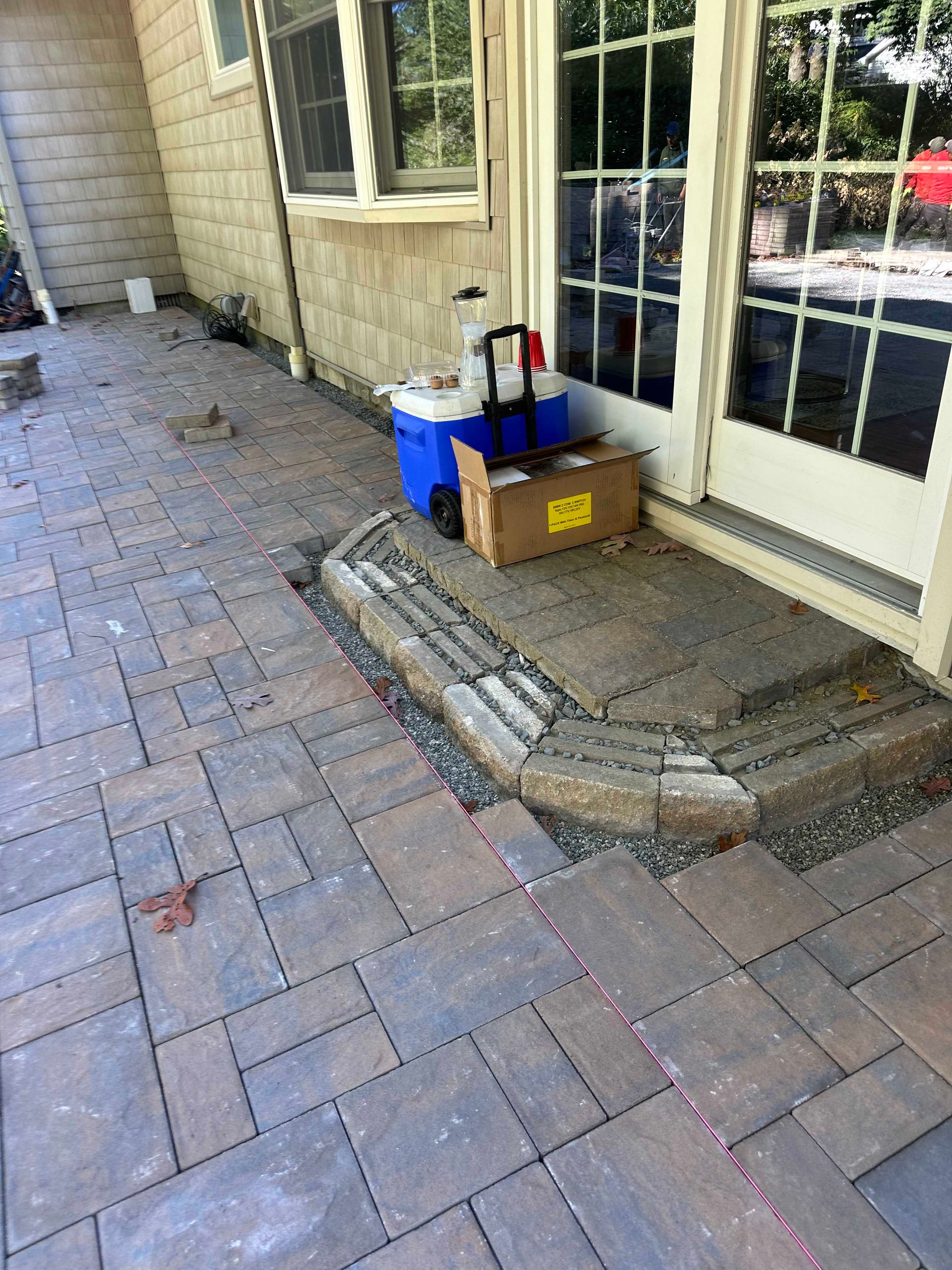 Brick patio with curved step leading to a door; blue cooler, cardboard box, and other materials sit near the door.