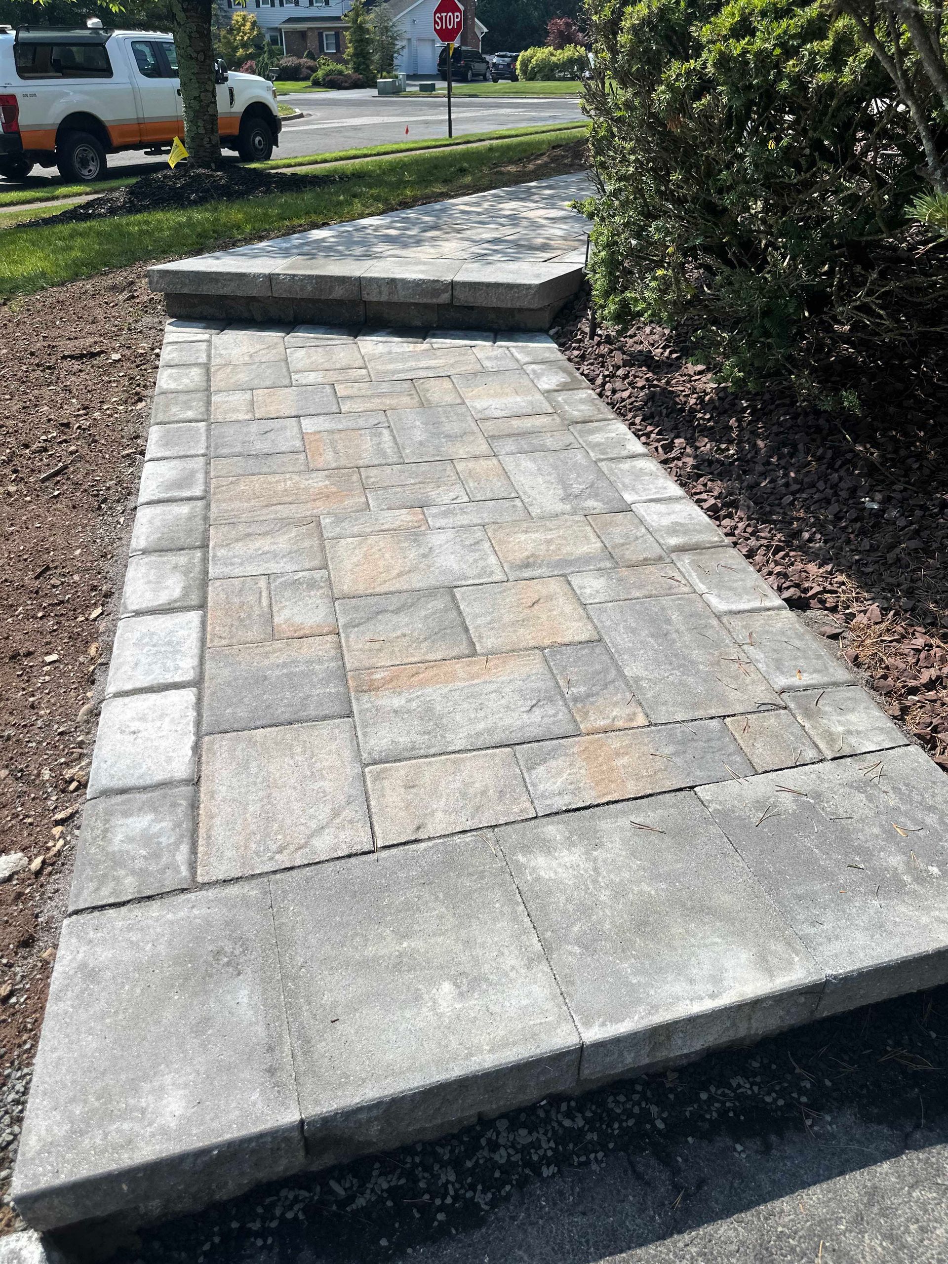 Stone pathway with steps, leading toward a bush, beside mulch and a lawn.
