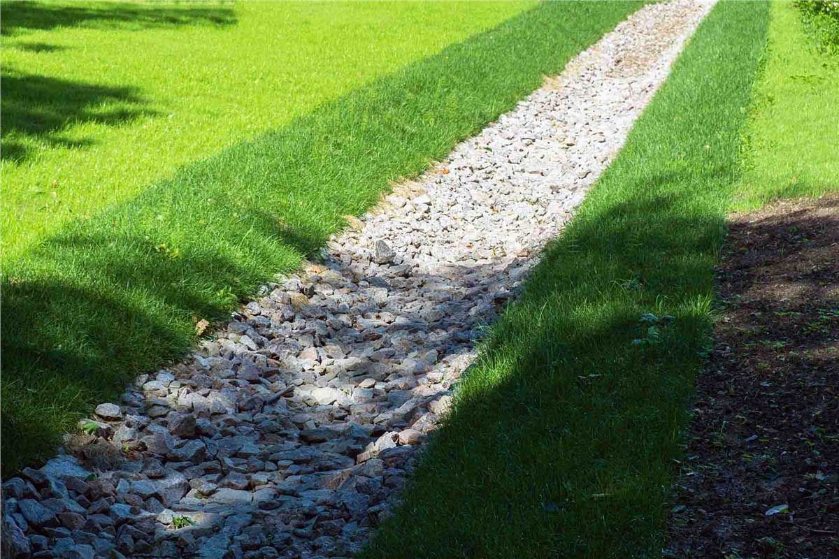 Gravel-filled drainage channel bordered by green grass in an outdoor setting.