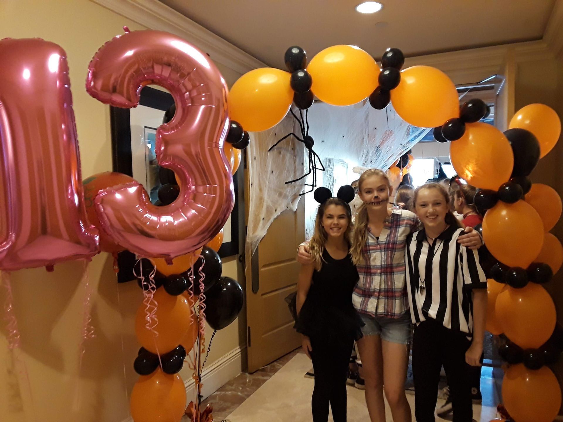 Three girls are posing for a picture in front of balloons and a pink number 13 balloon.