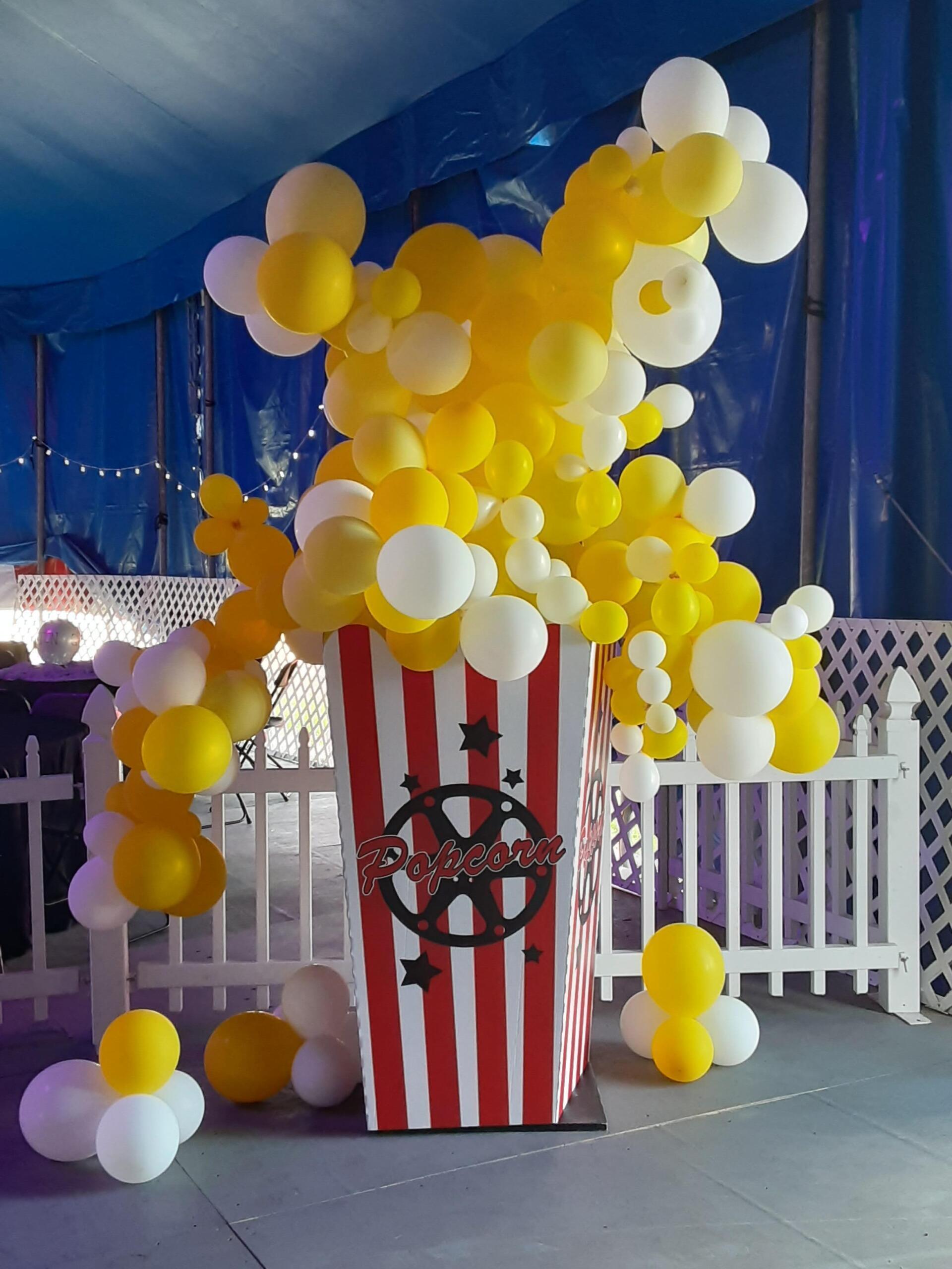 A box of popcorn is surrounded by yellow and white balloons