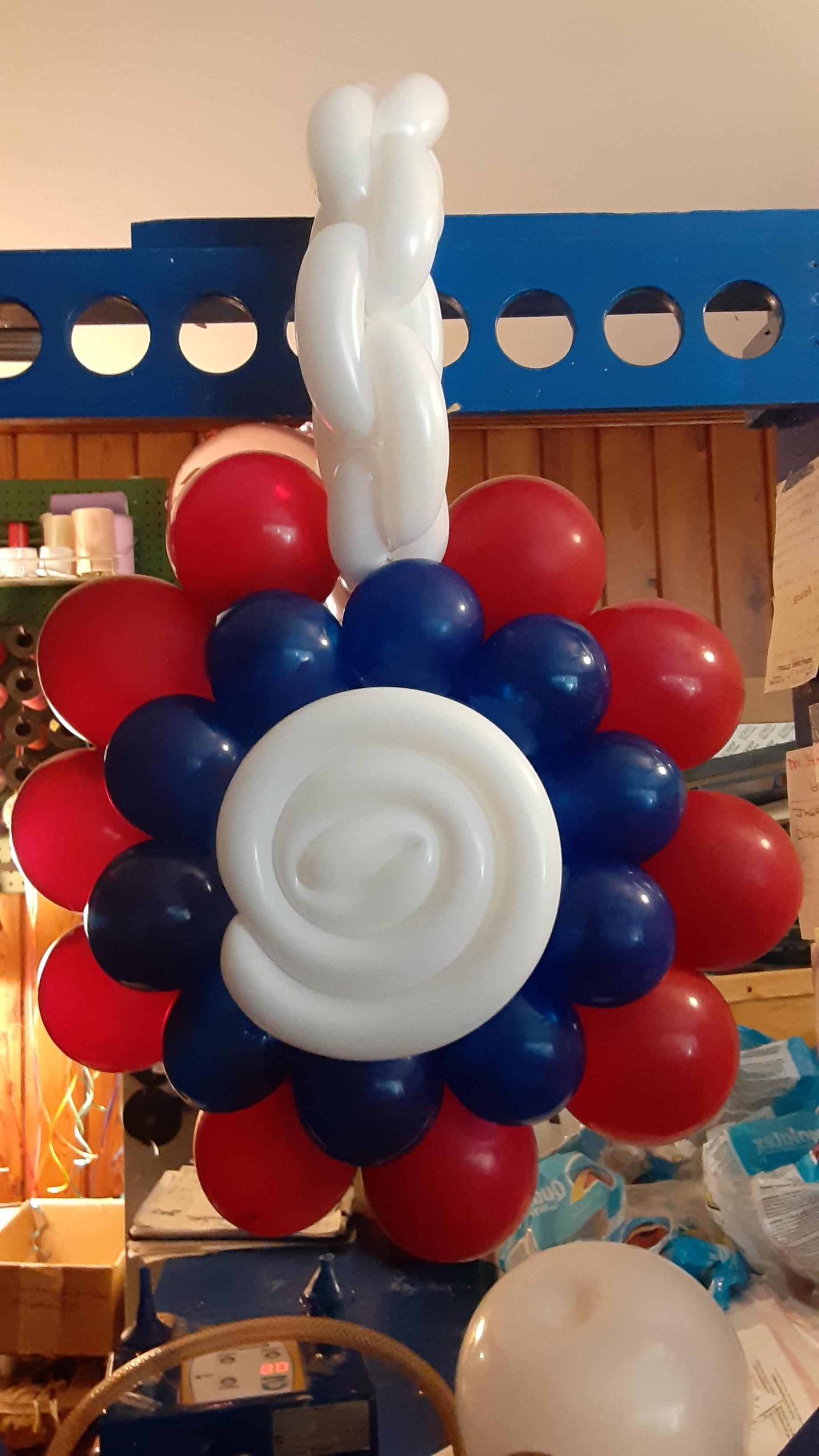 A bunch of red white and blue balloons with a white balloon in the middle