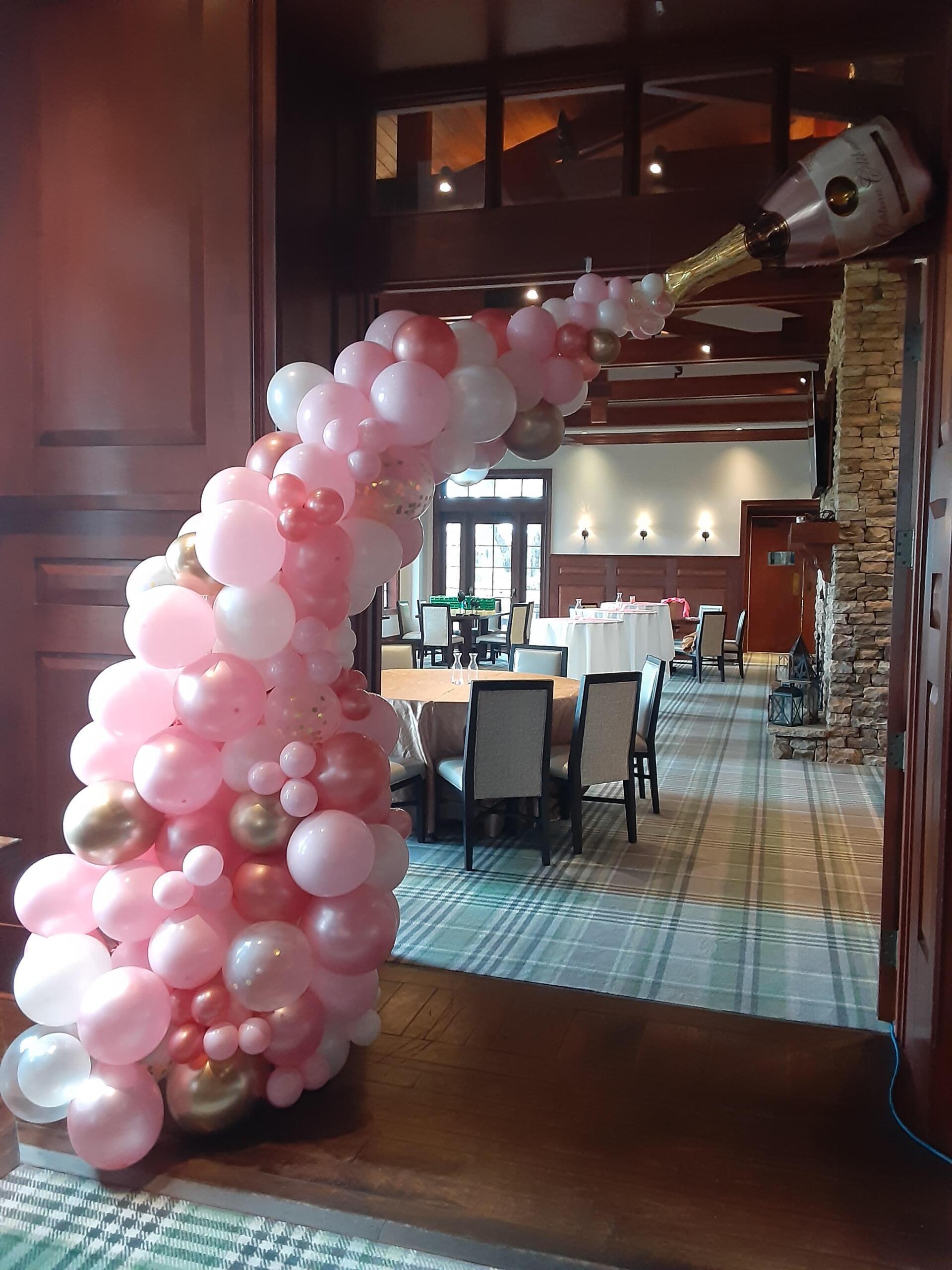 A room filled with pink and gold balloons and a bottle of champagne.
