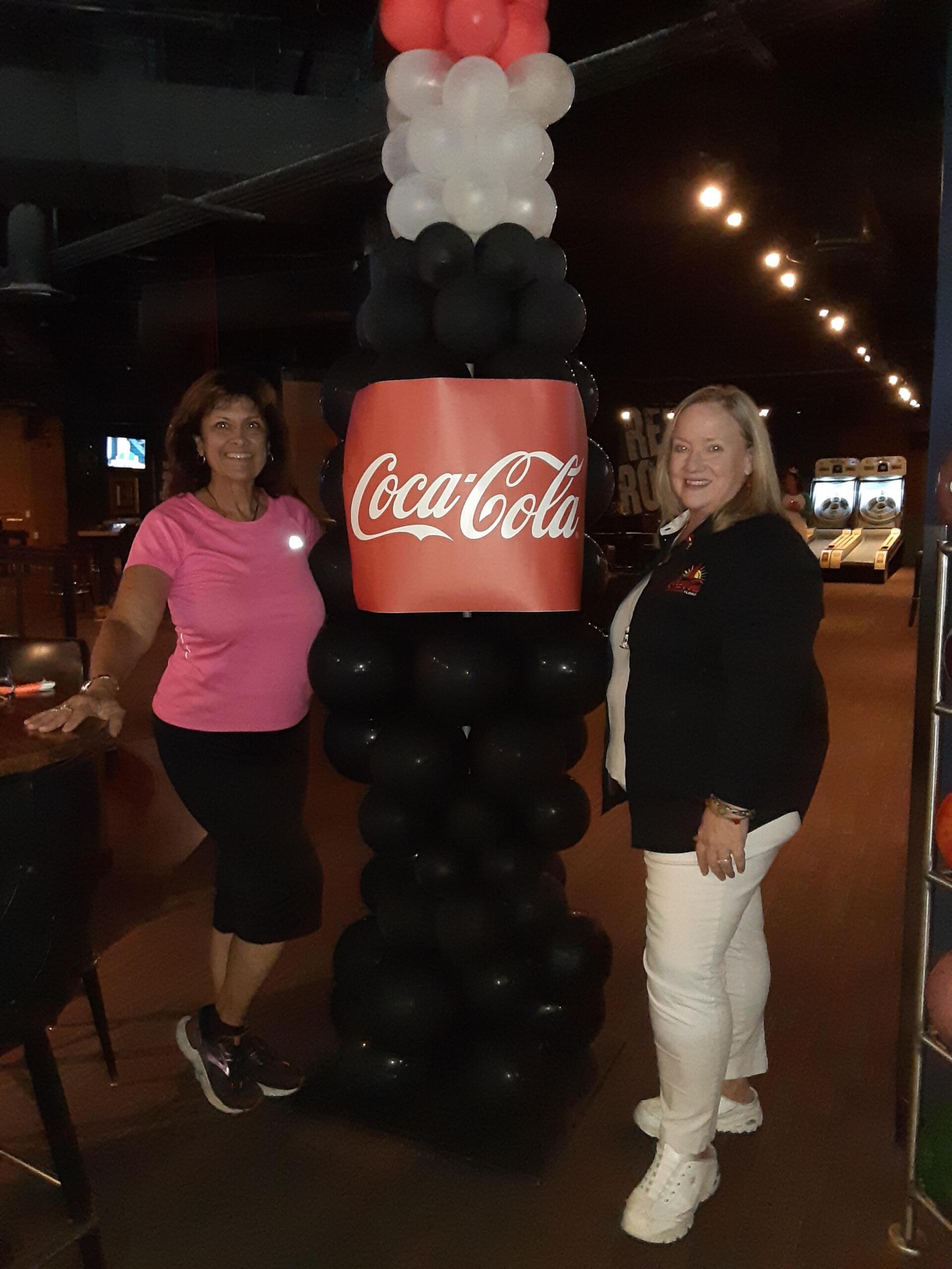 Two women standing in front of a coca cola balloon display