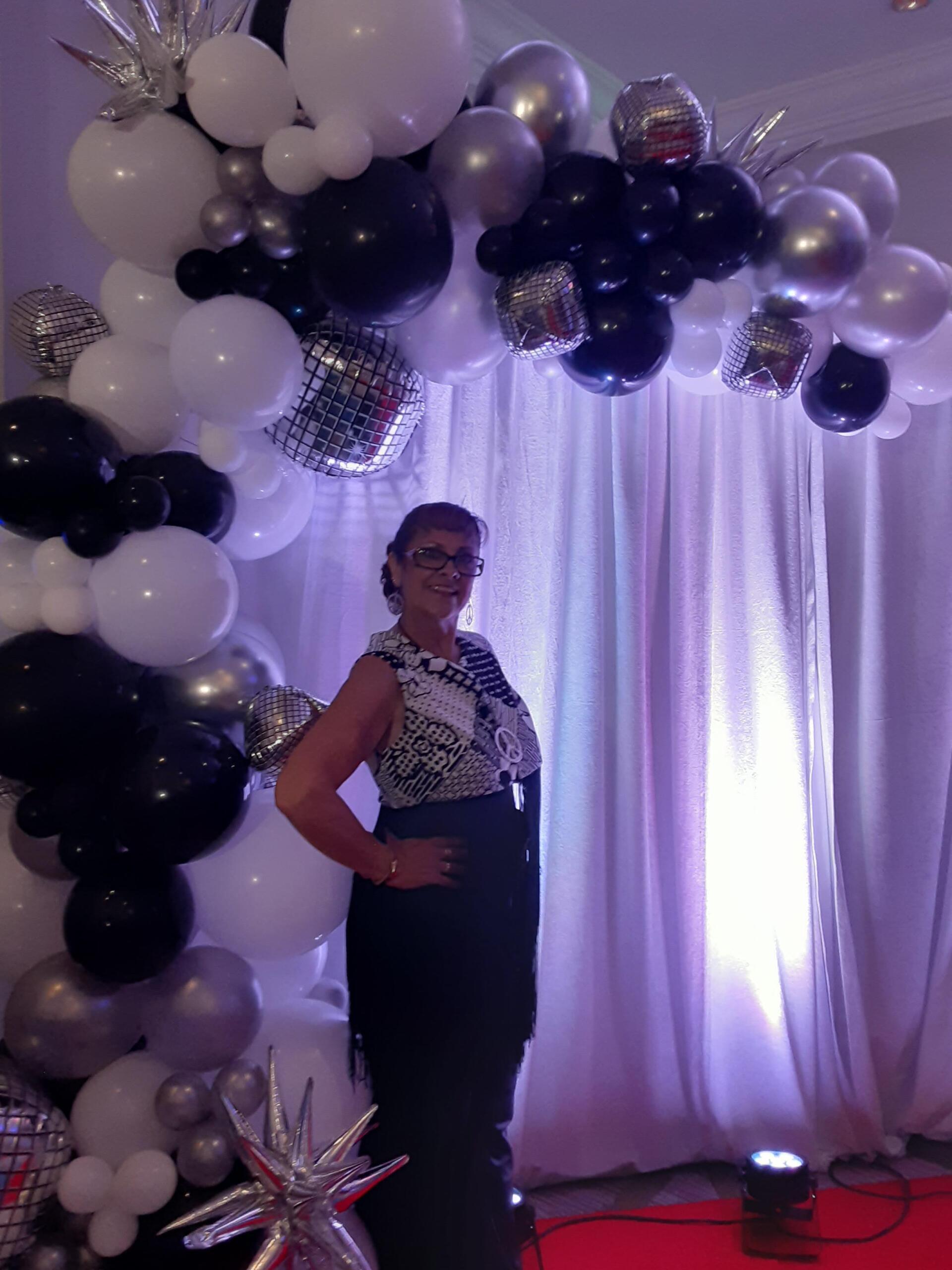 A woman in a black dress is standing in front of a balloon arch.