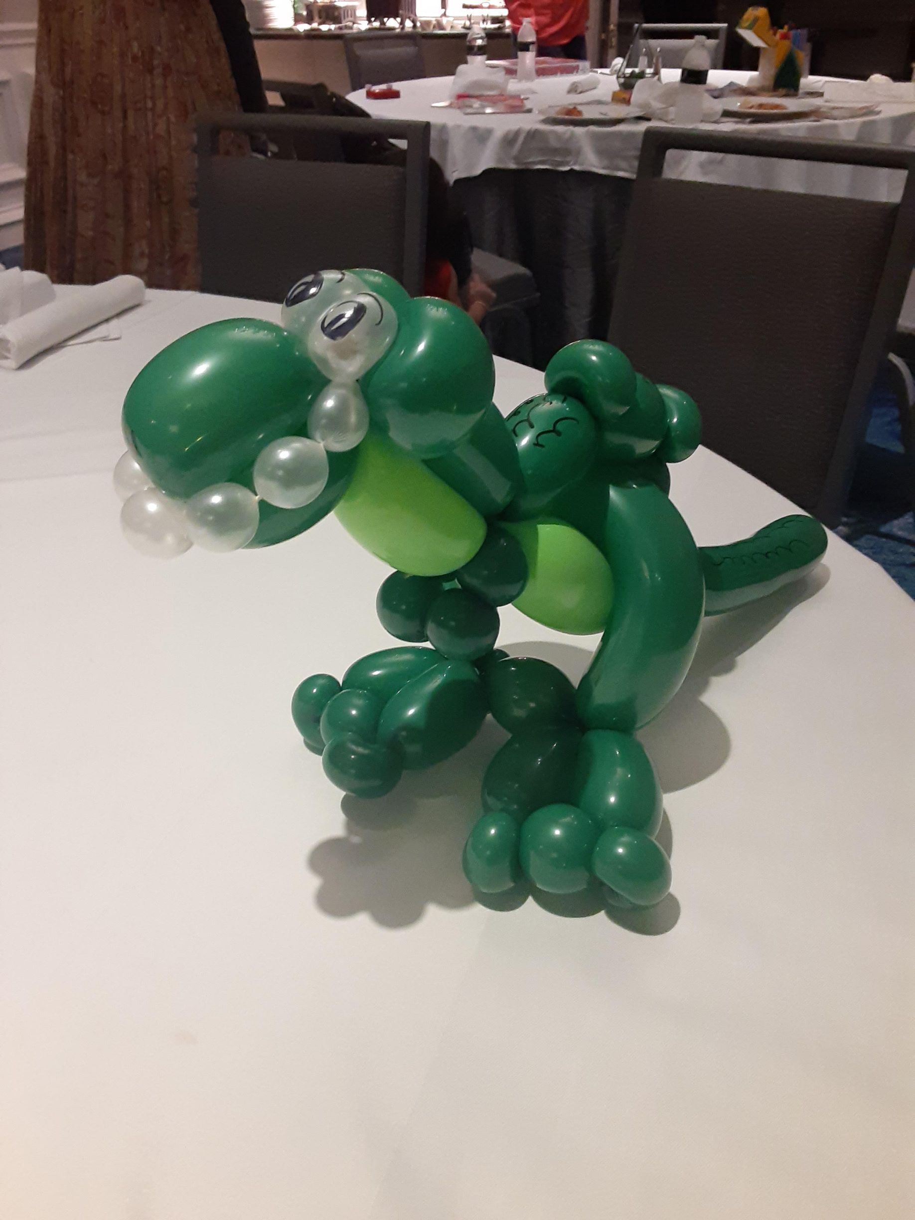 A green balloon dinosaur is sitting on a white table.