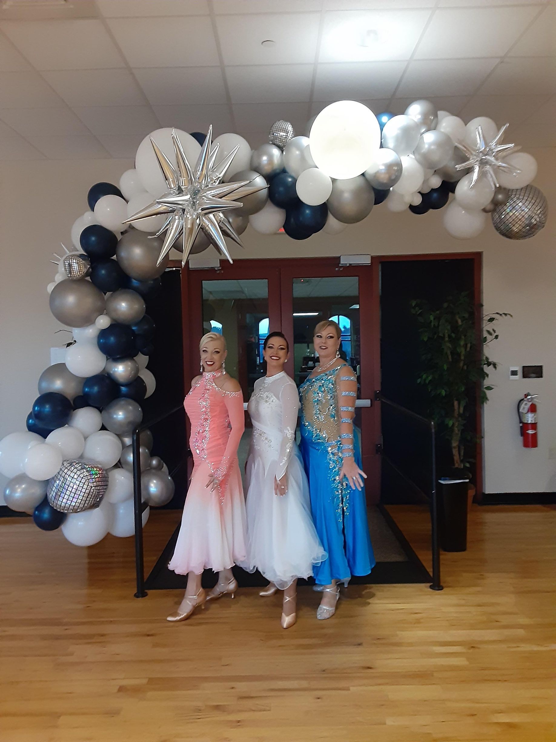 Three women are posing for a picture in front of a balloon arch.