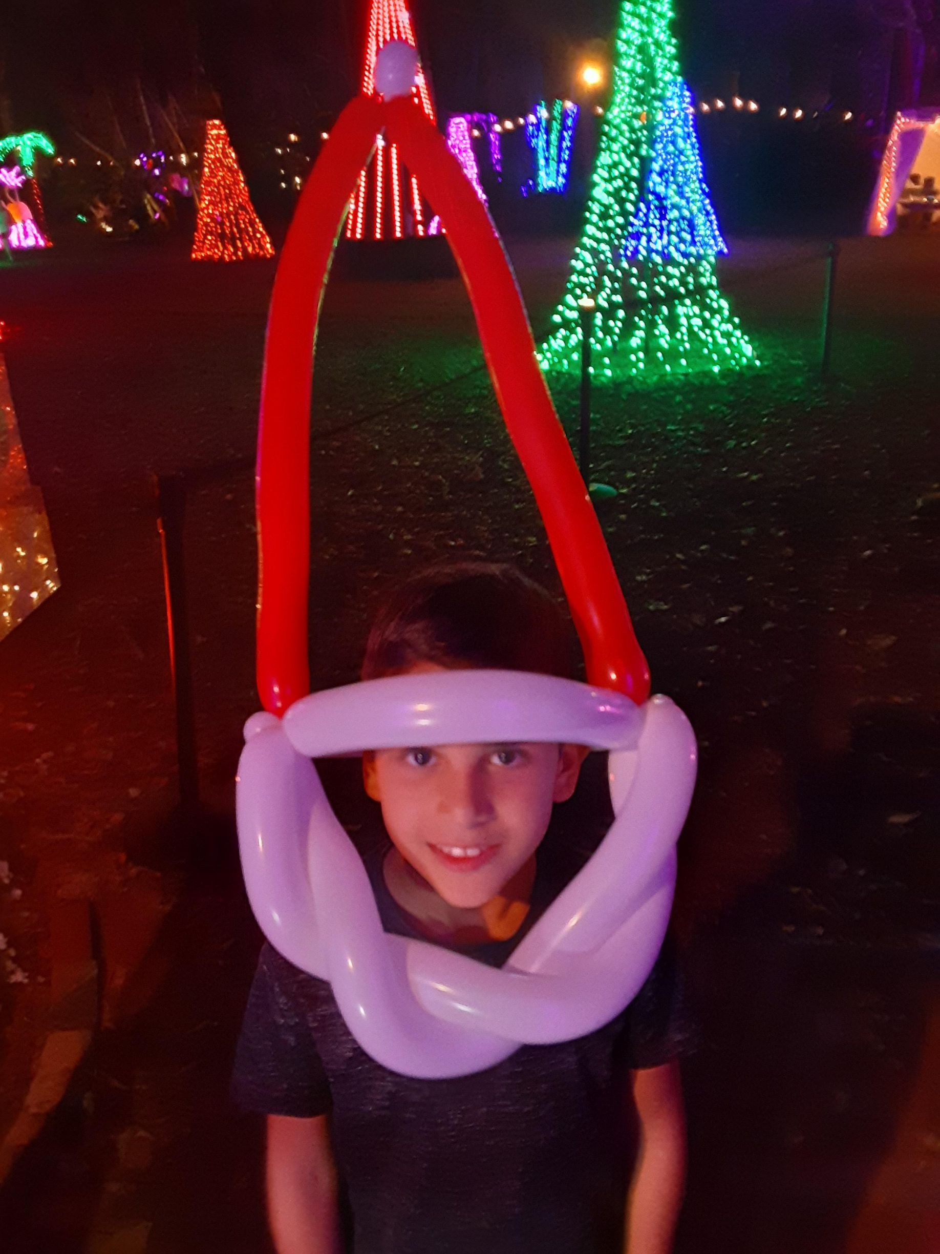 A young boy wearing a santa hat made of balloons
