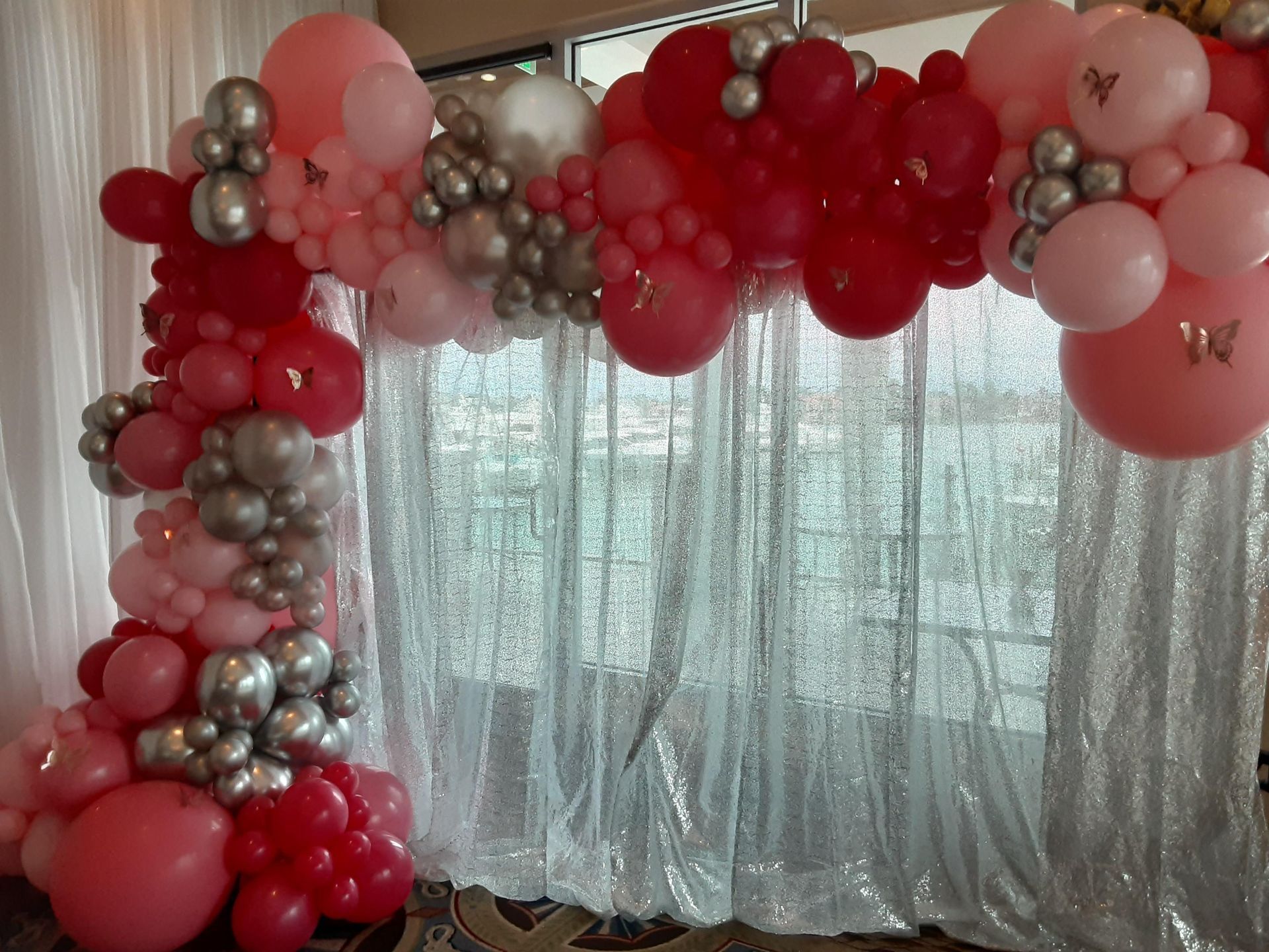 A bunch of pink and silver balloons are hanging from a white curtain.
