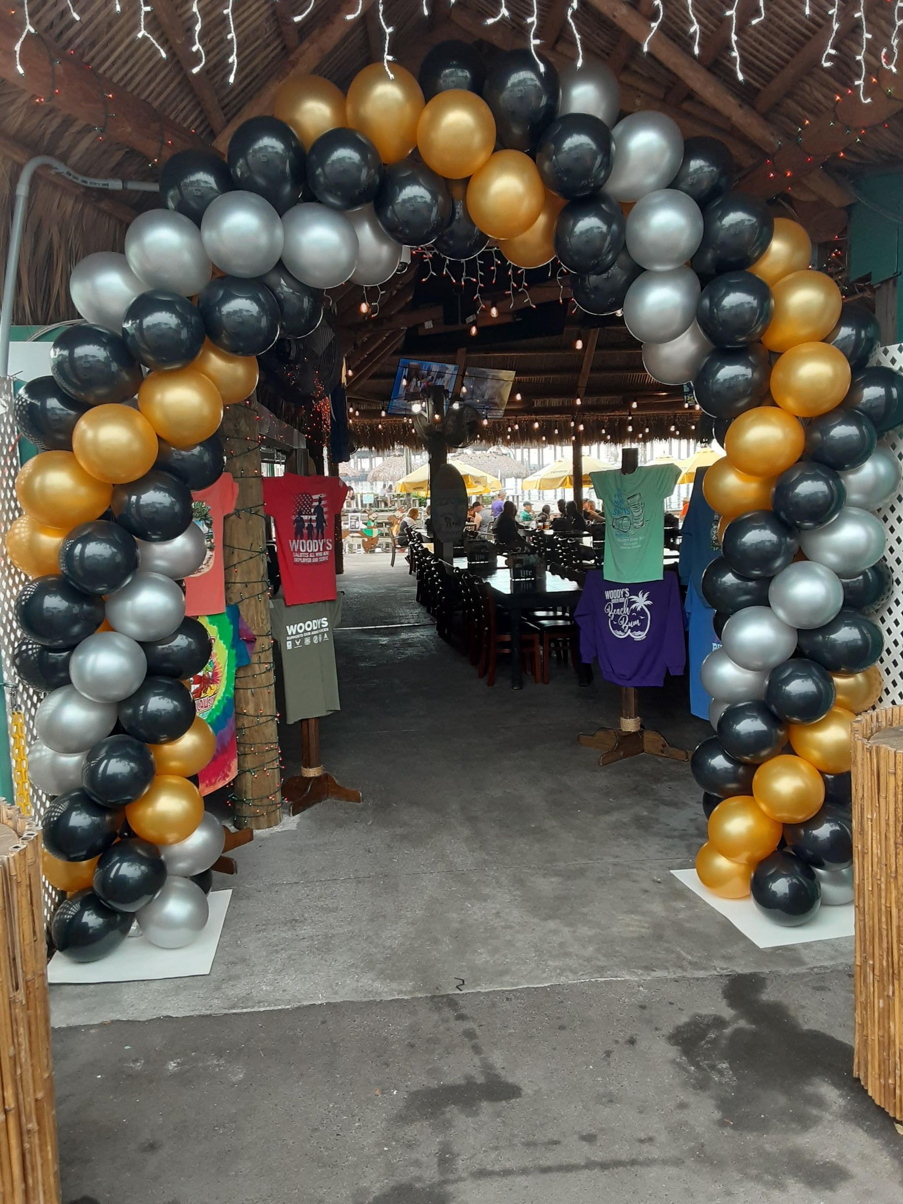 A large arch made of gold , silver and black balloons
