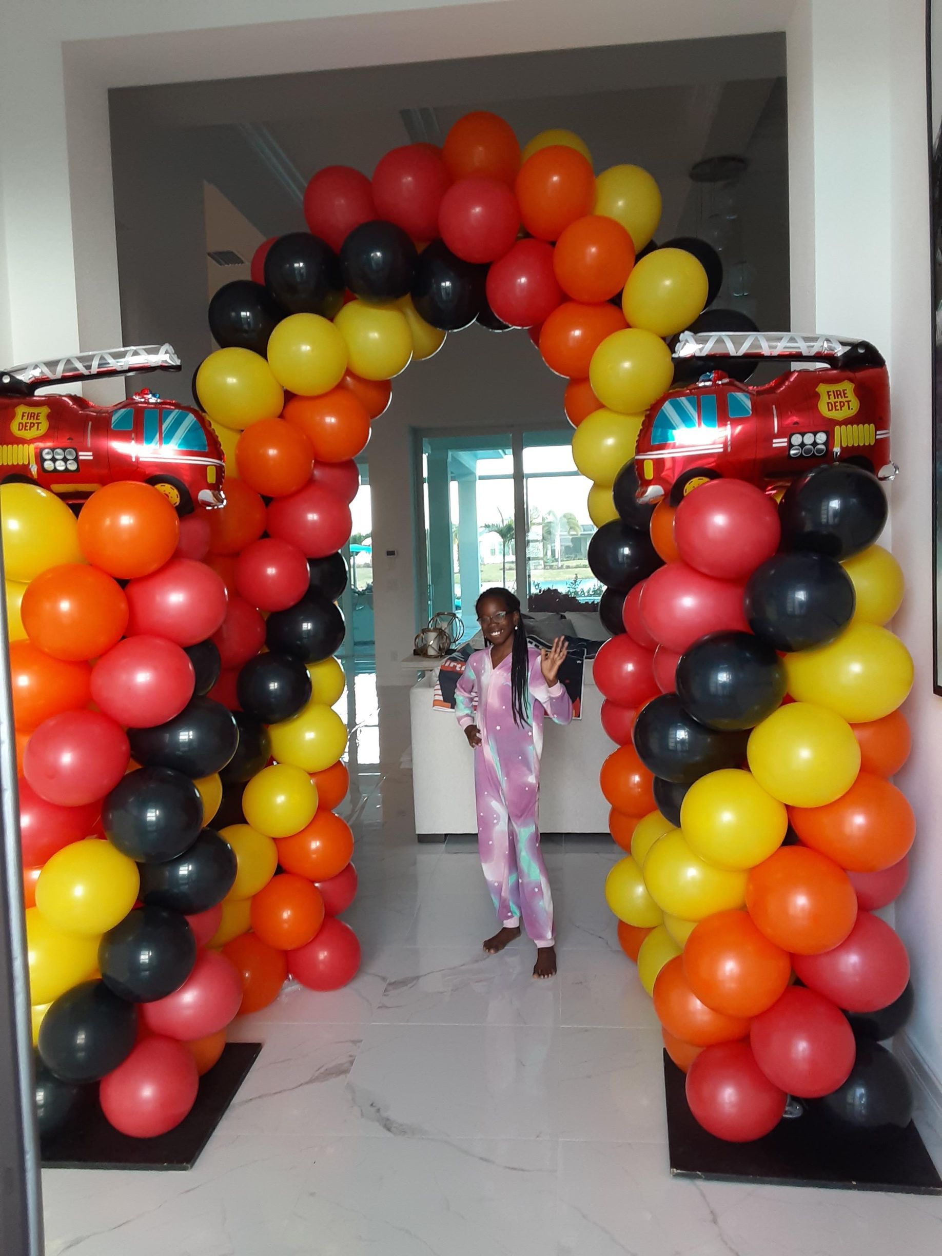 A girl is standing under an arch of balloons