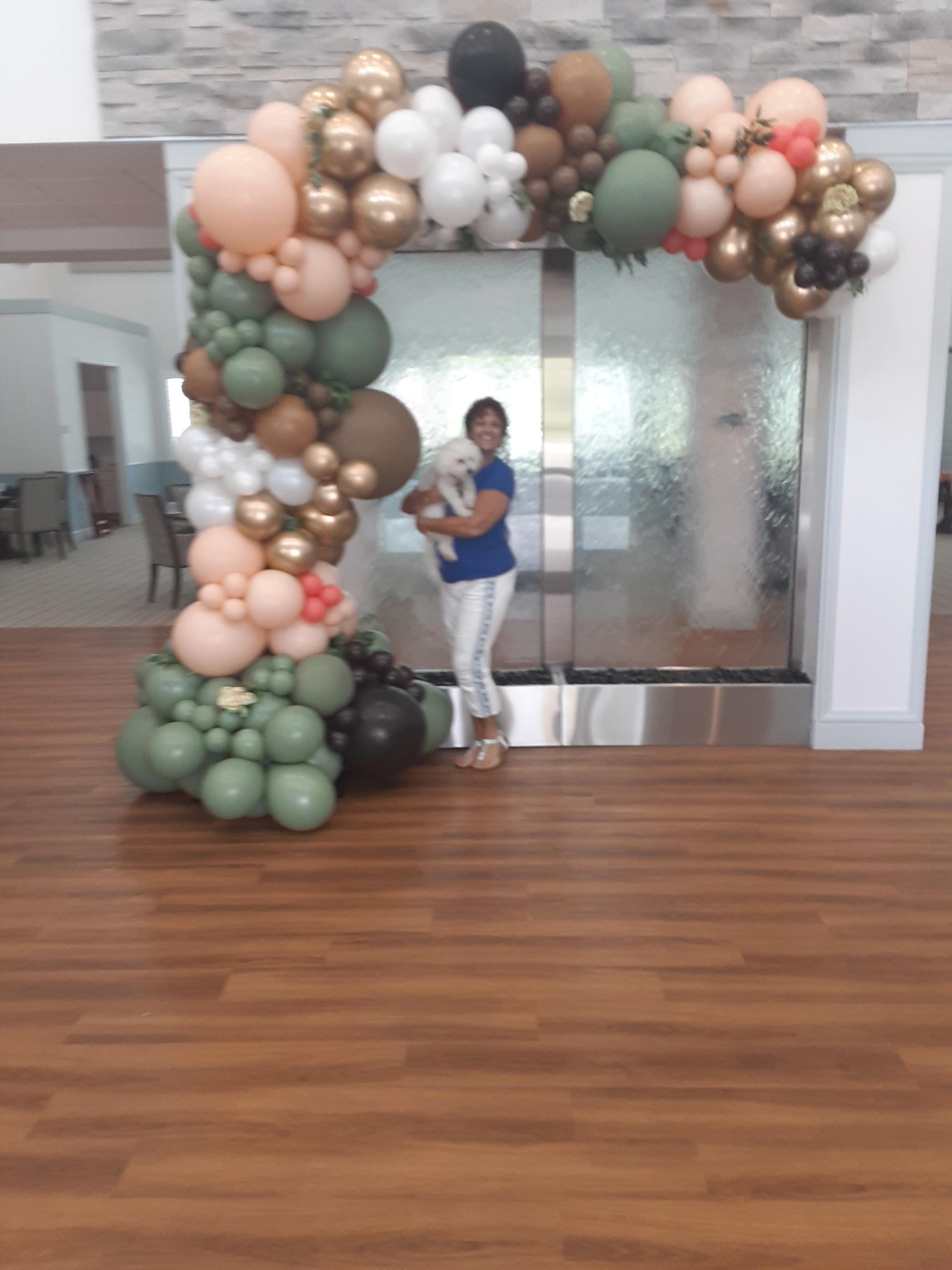A woman is holding a dog in front of a balloon arch.
