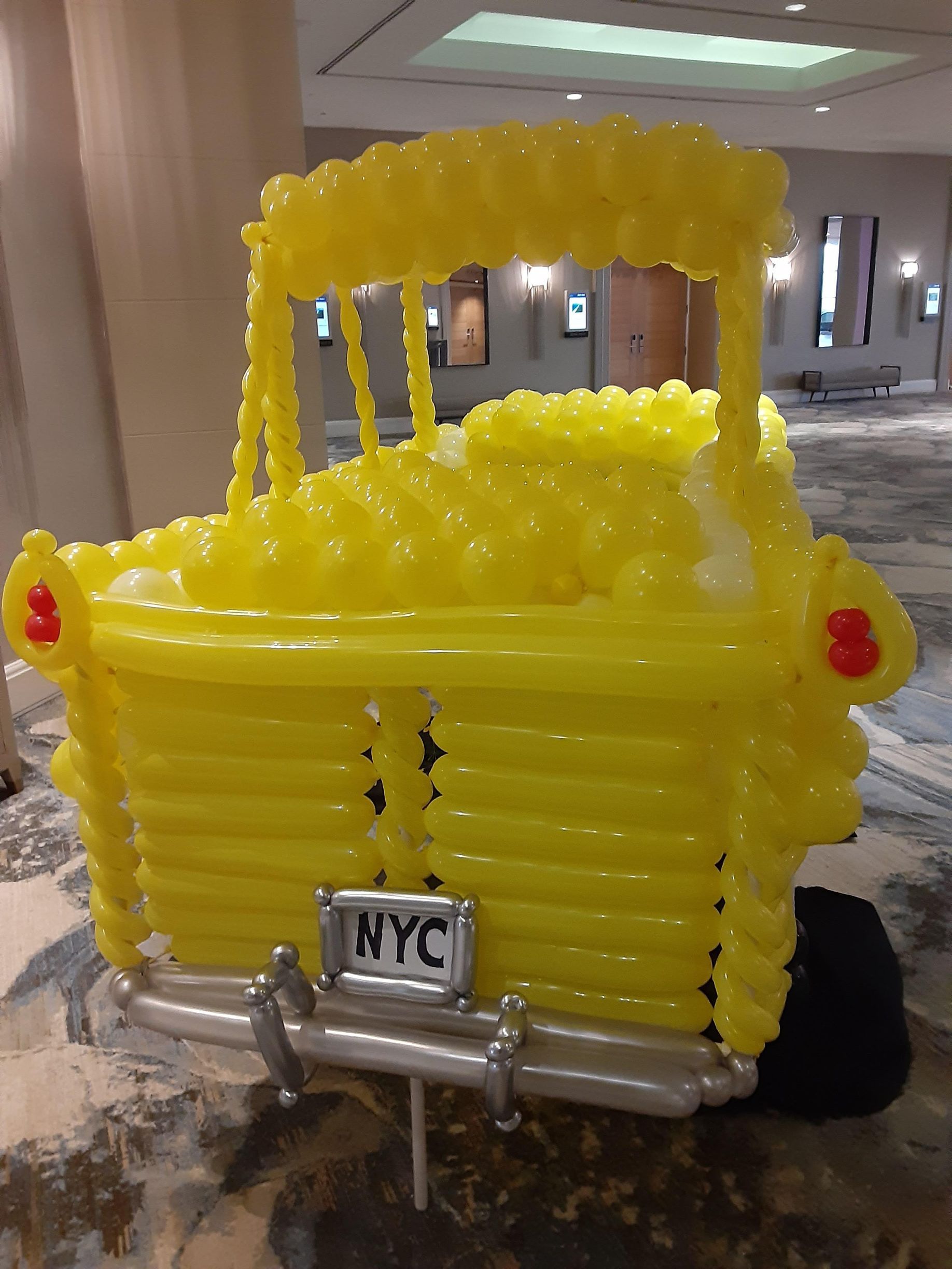 A yellow truck made out of balloons with a nyc license plate