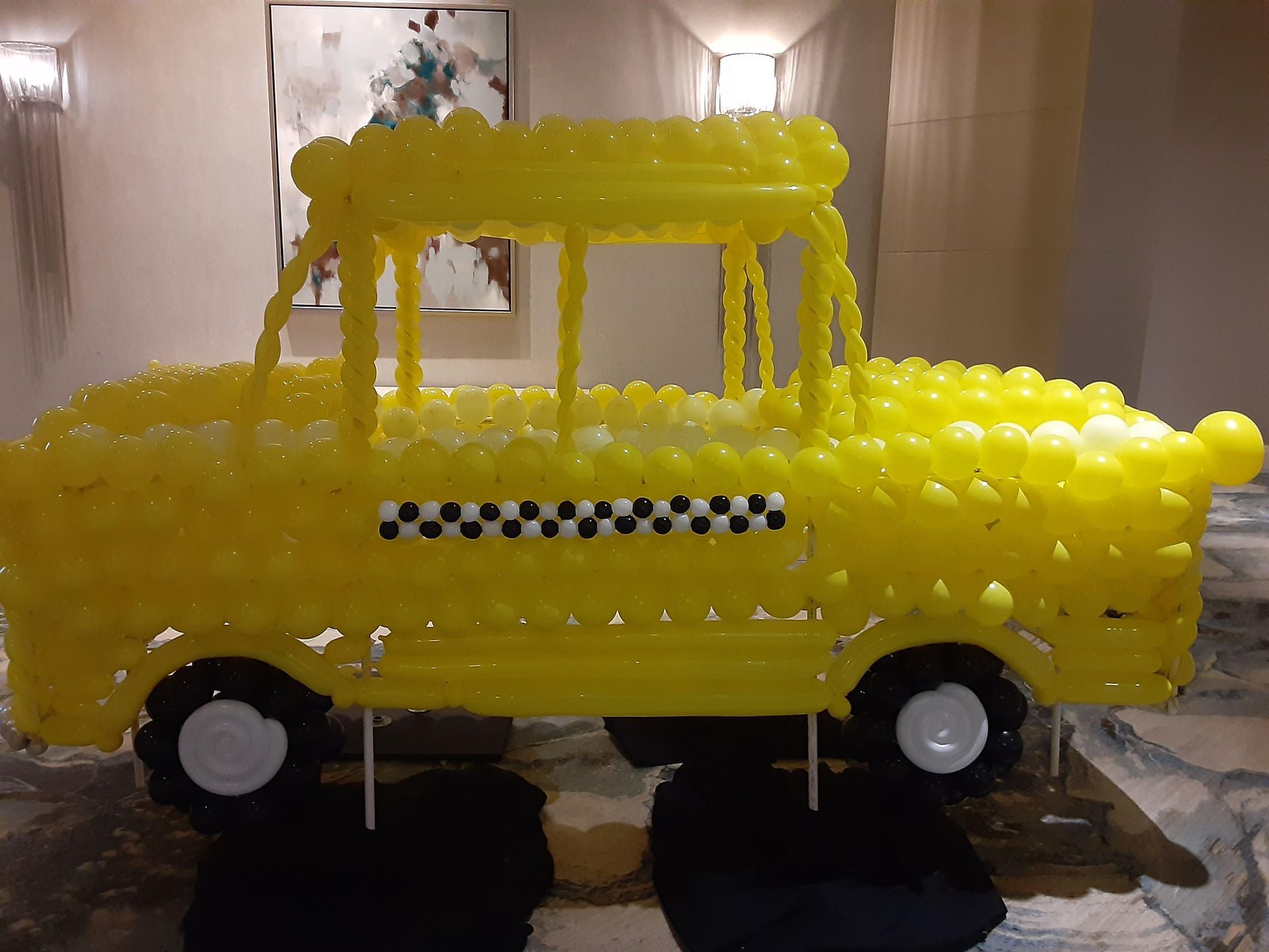 A yellow taxi made out of balloons in a room