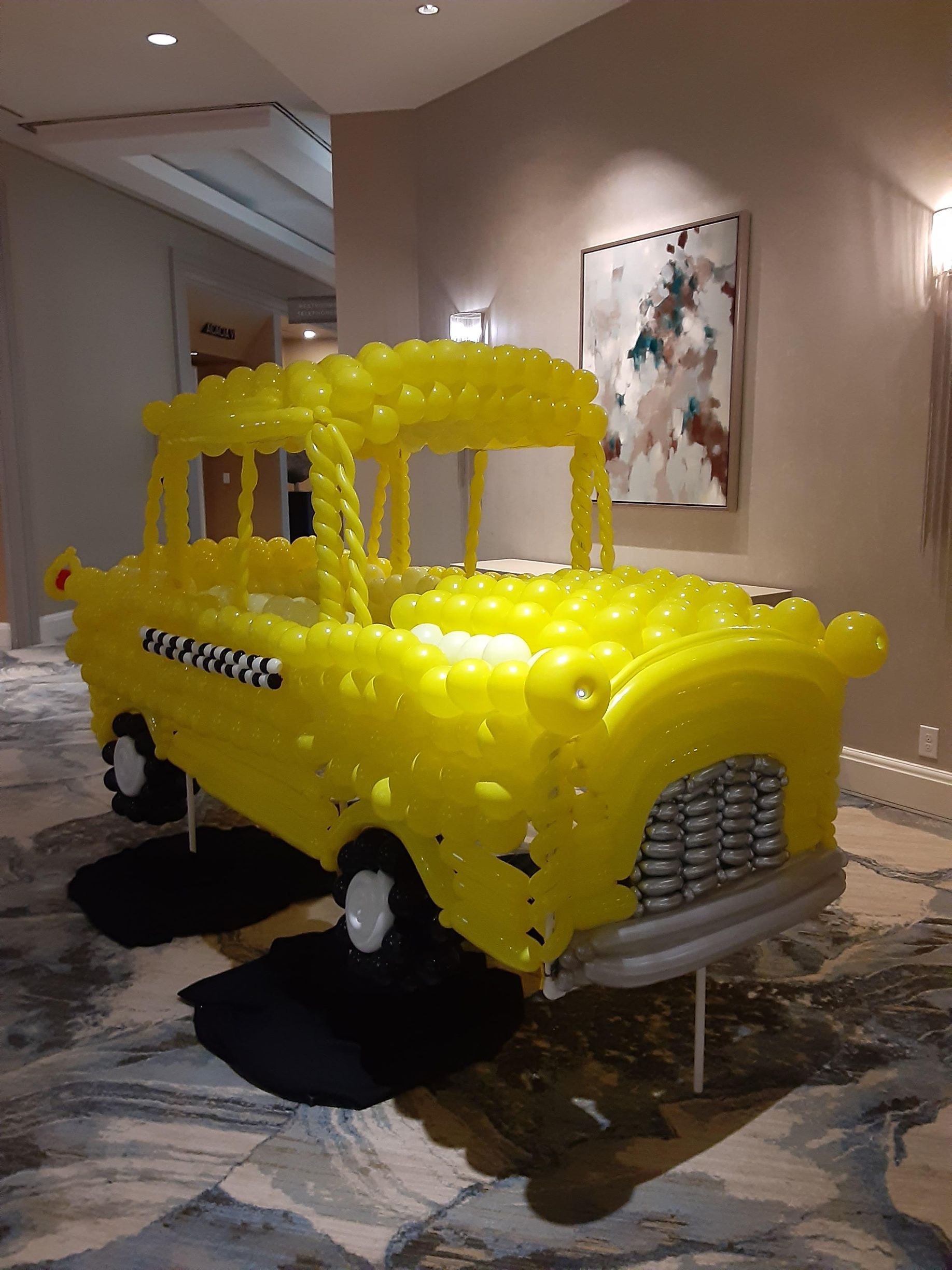A yellow taxi cab made out of balloons in a room.