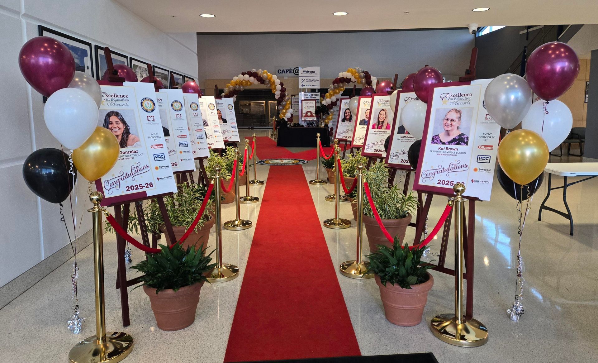 Red carpet entrance with signs, balloons, and potted plants.