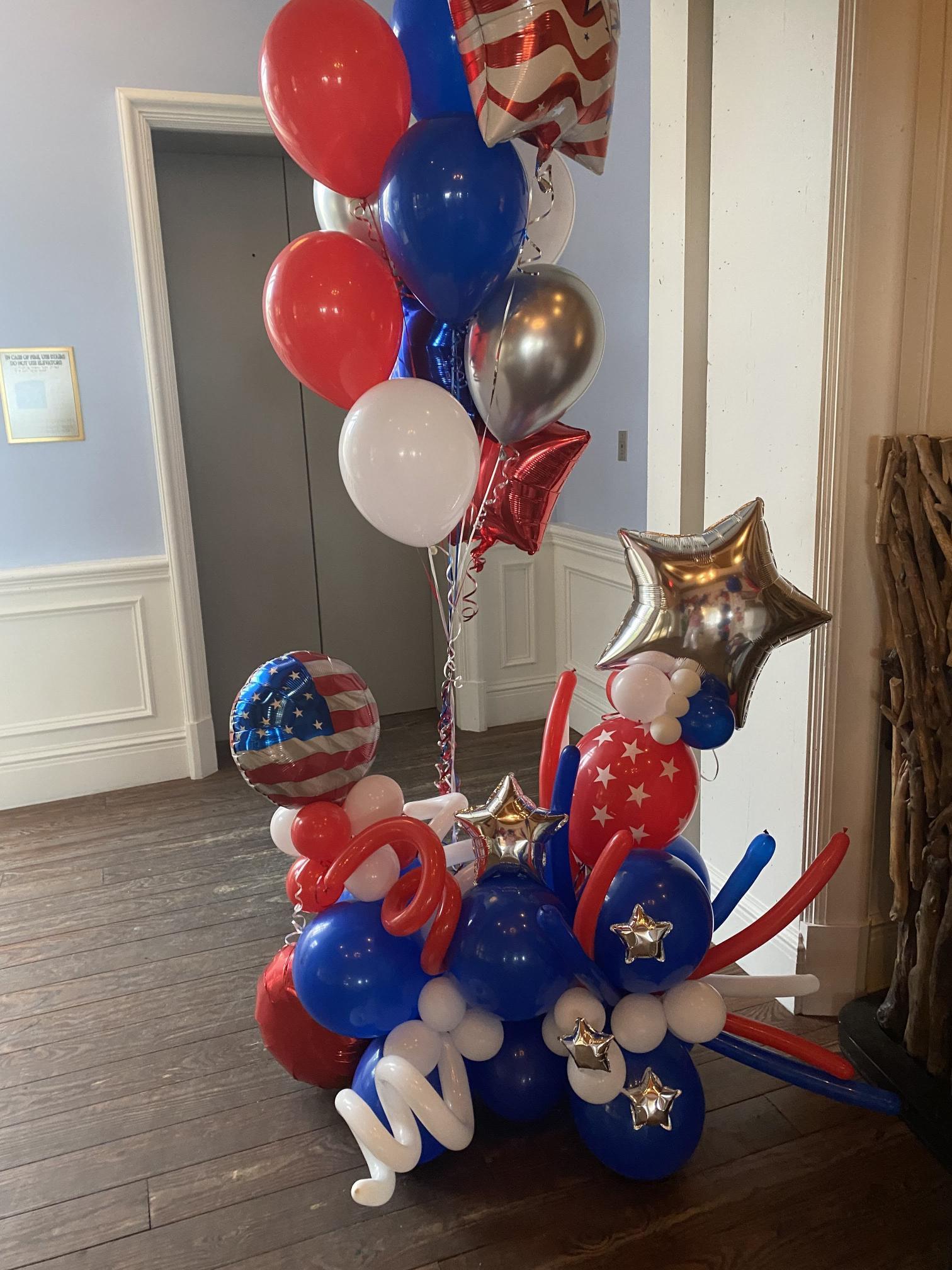 A bunch of red , white and blue balloons are sitting on a wooden floor.