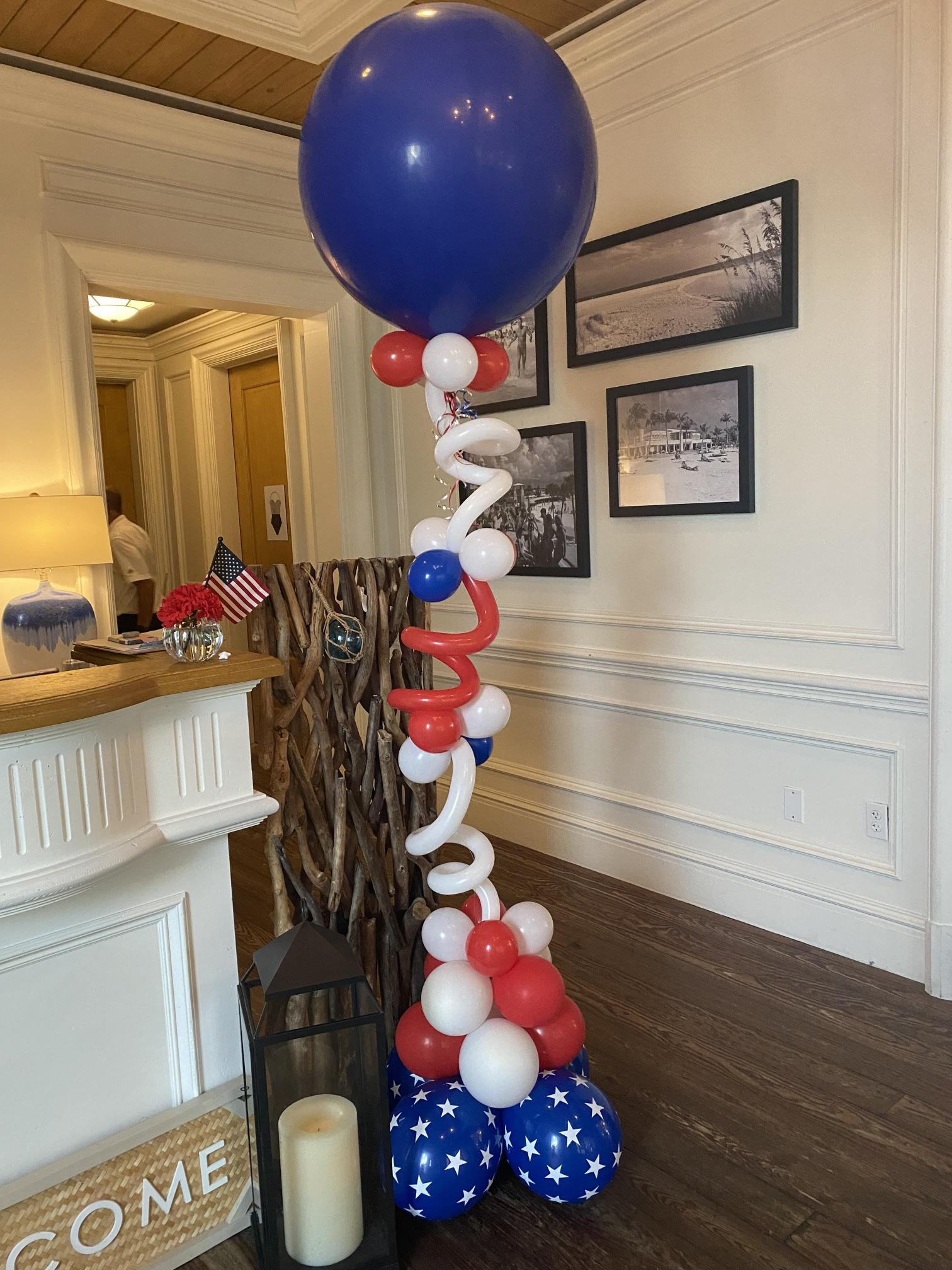 A large blue balloon is surrounded by red , white and blue balloons in a room.