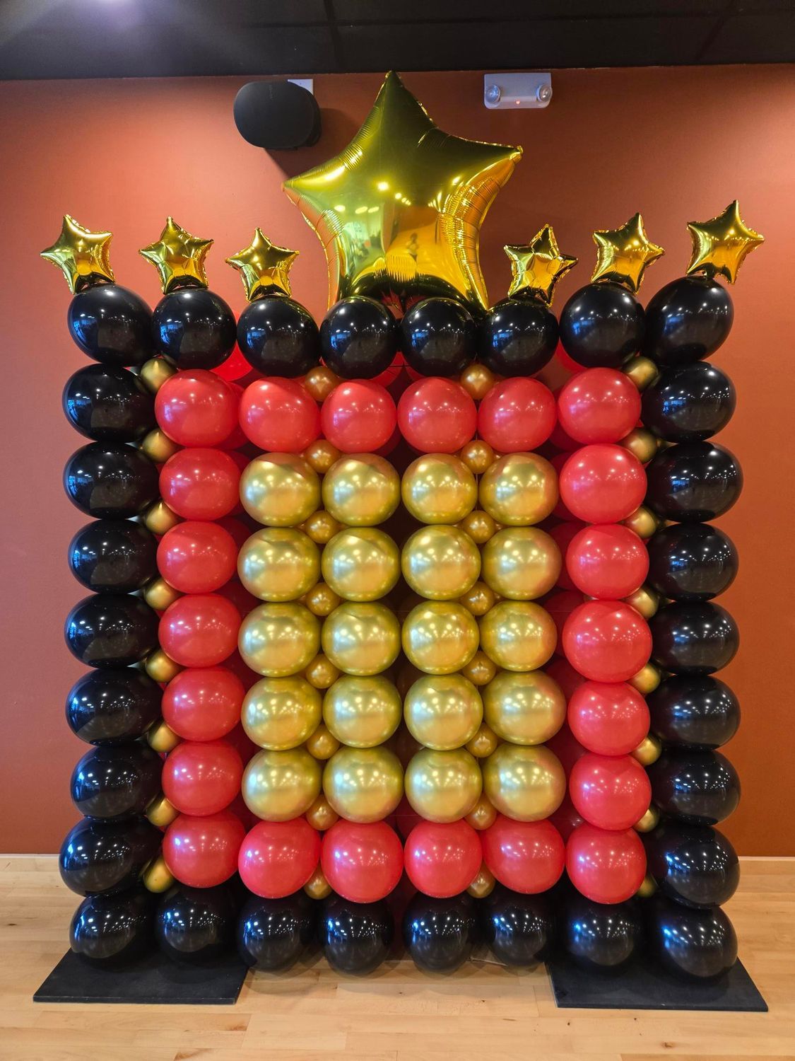 Balloon wall with black, red, and gold balloons. Gold star balloons adorn the top.