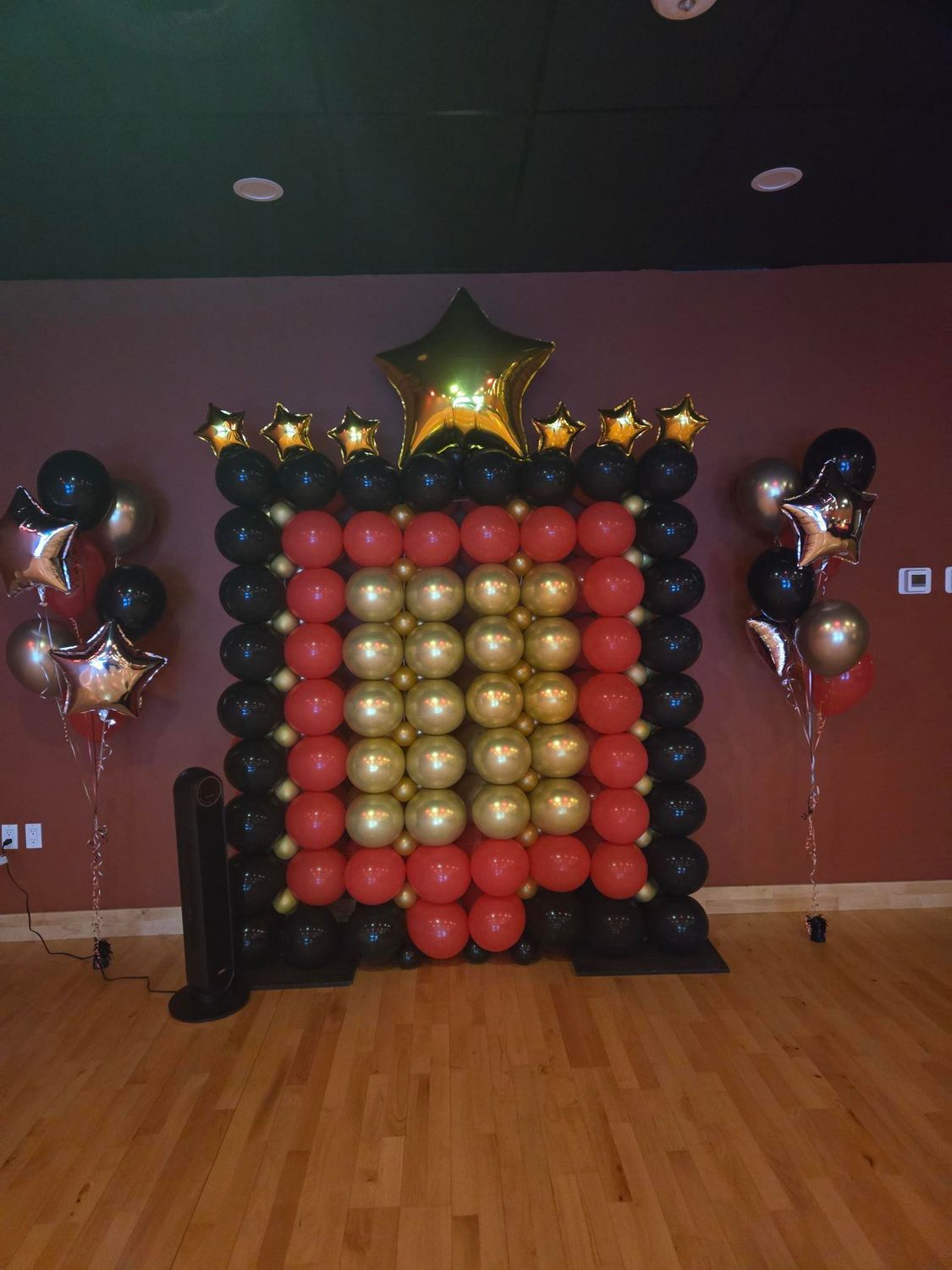 Balloon arch backdrop: black, red, gold balloons, star accents. Party setting.