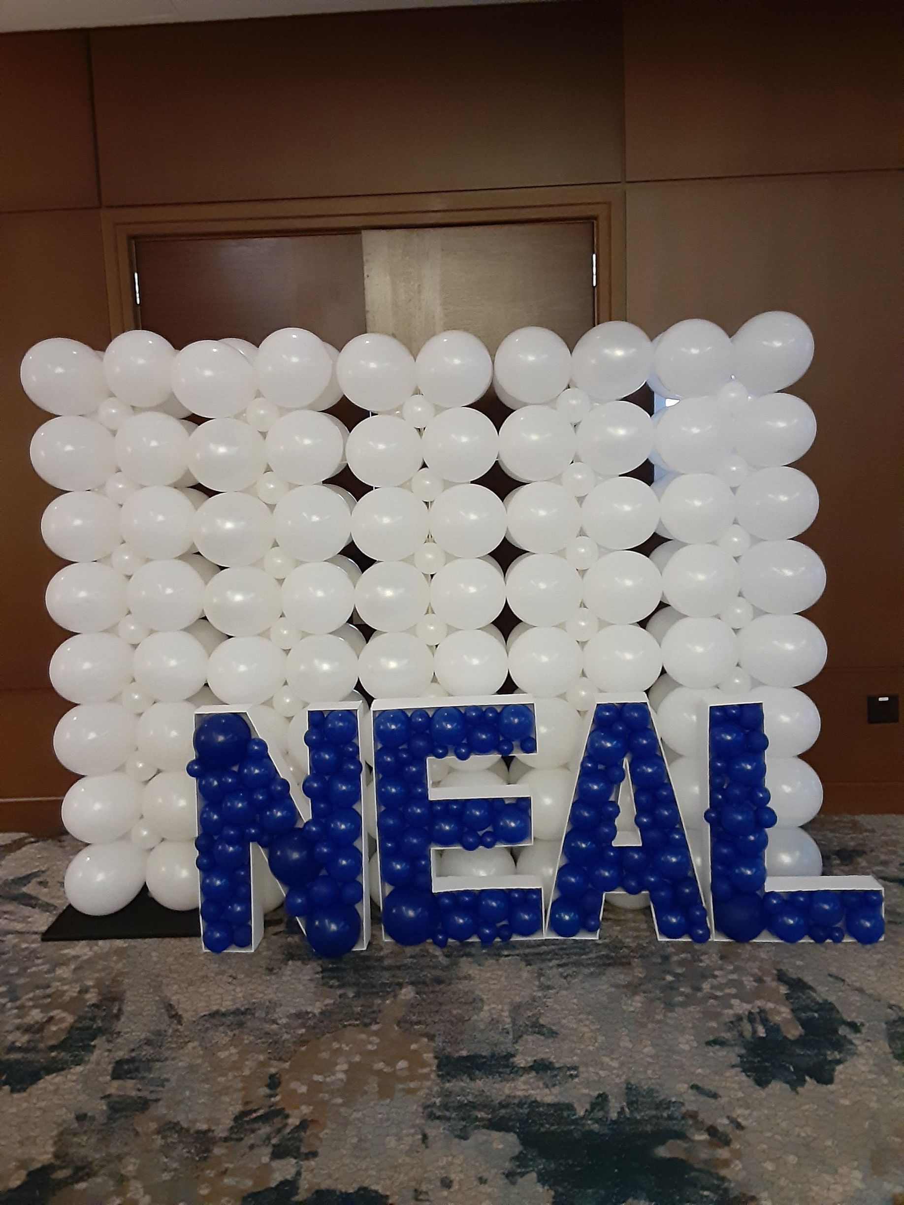 White balloon wall backdrop with blue balloon letters spelling